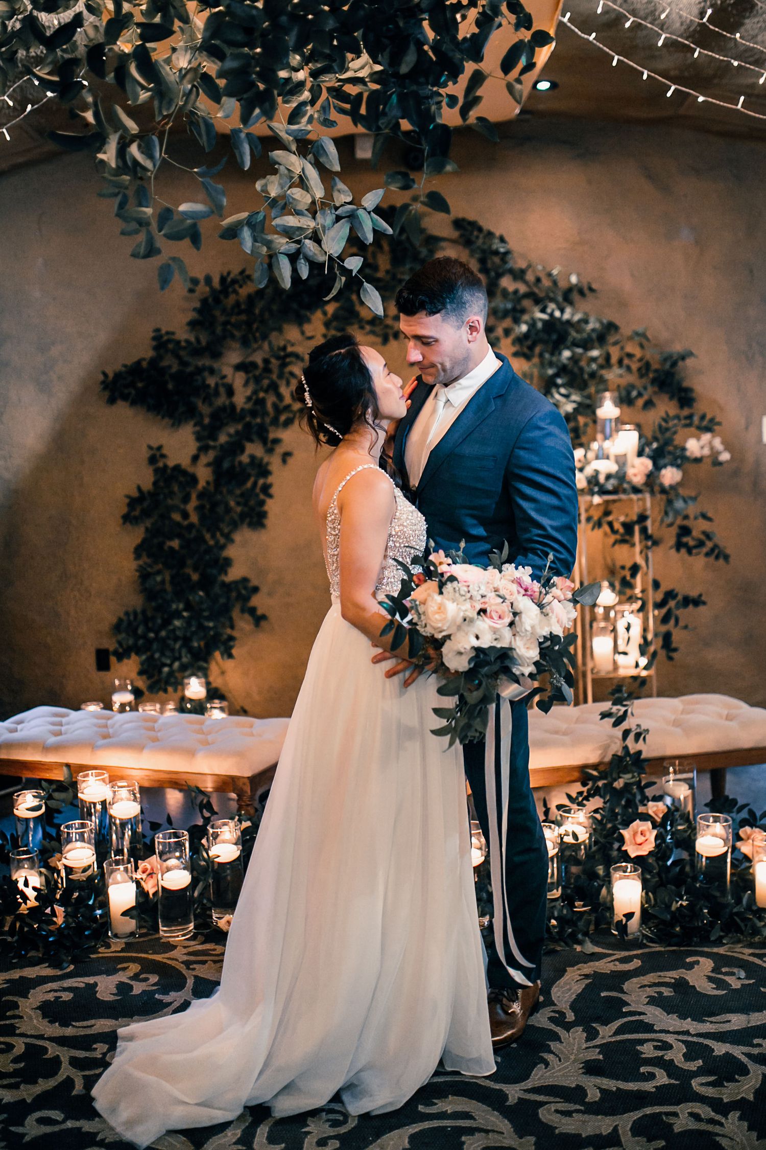 Bride and groom share a romantic moment surrounded by candles and floral arrangements at an elegant wedding reception.