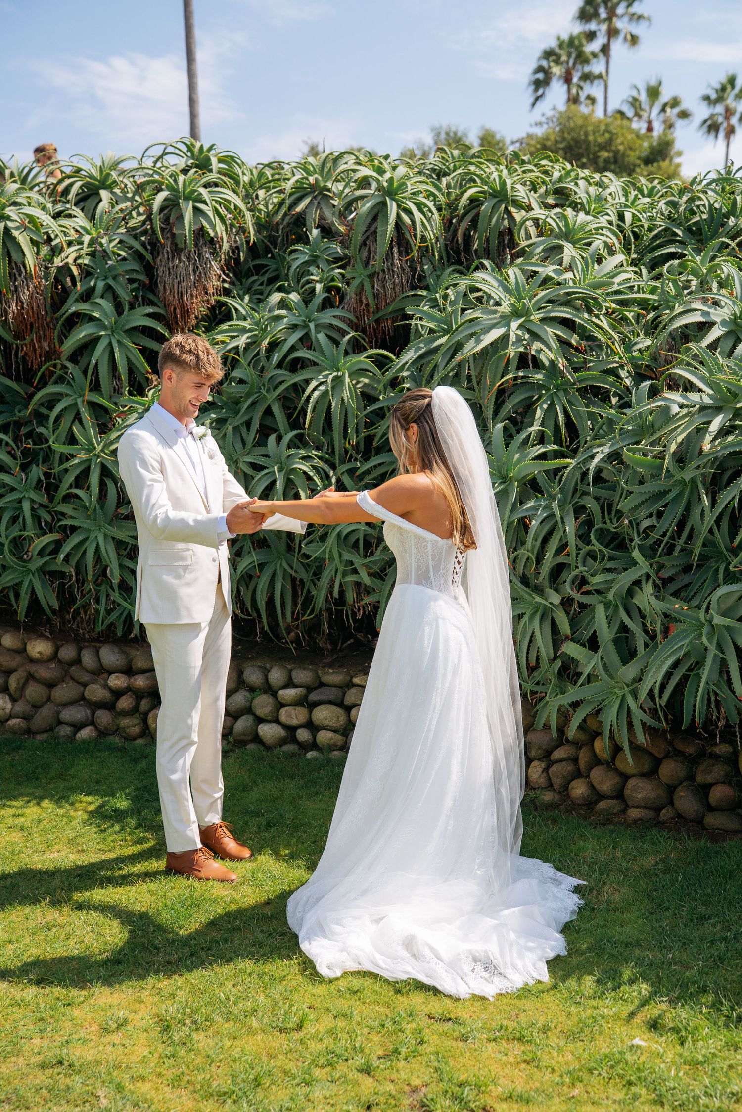 Bride and groom exchange private vows during first look in front of tropical garden hedge.
