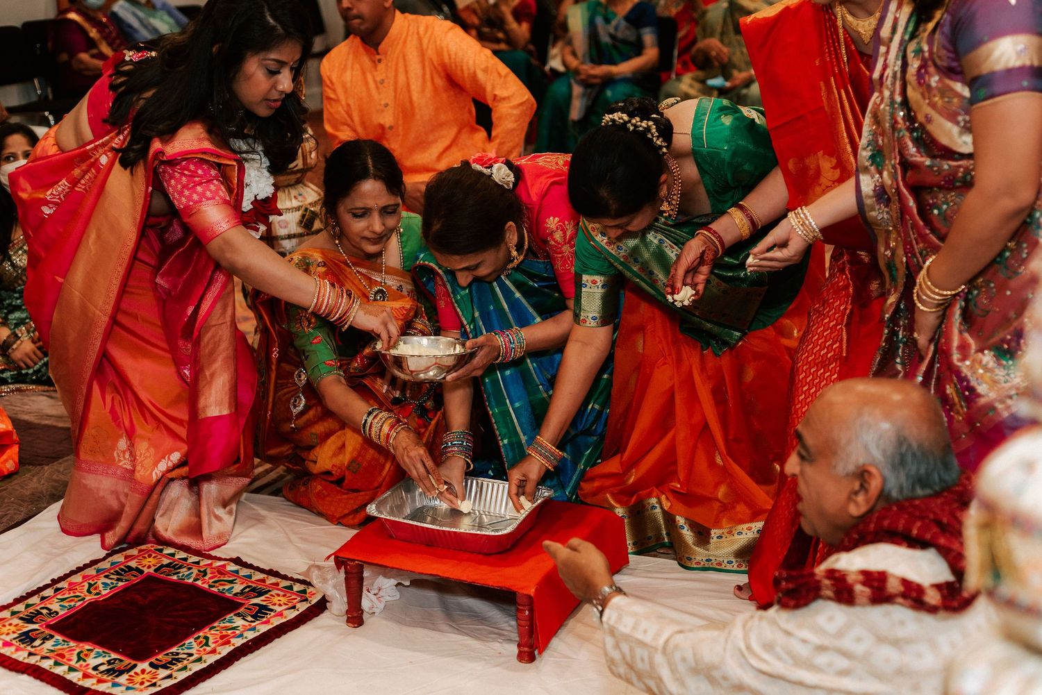 Family members in colorful sarees performing a traditional Hindu wedding ritual ceremony together indoors.