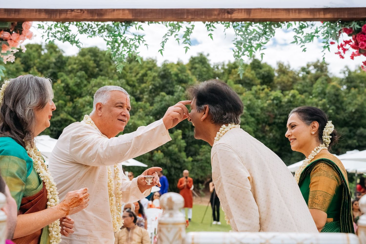 Joyful Indian wedding ceremony with guests exchanging blessings under a floral mandap outdoors.