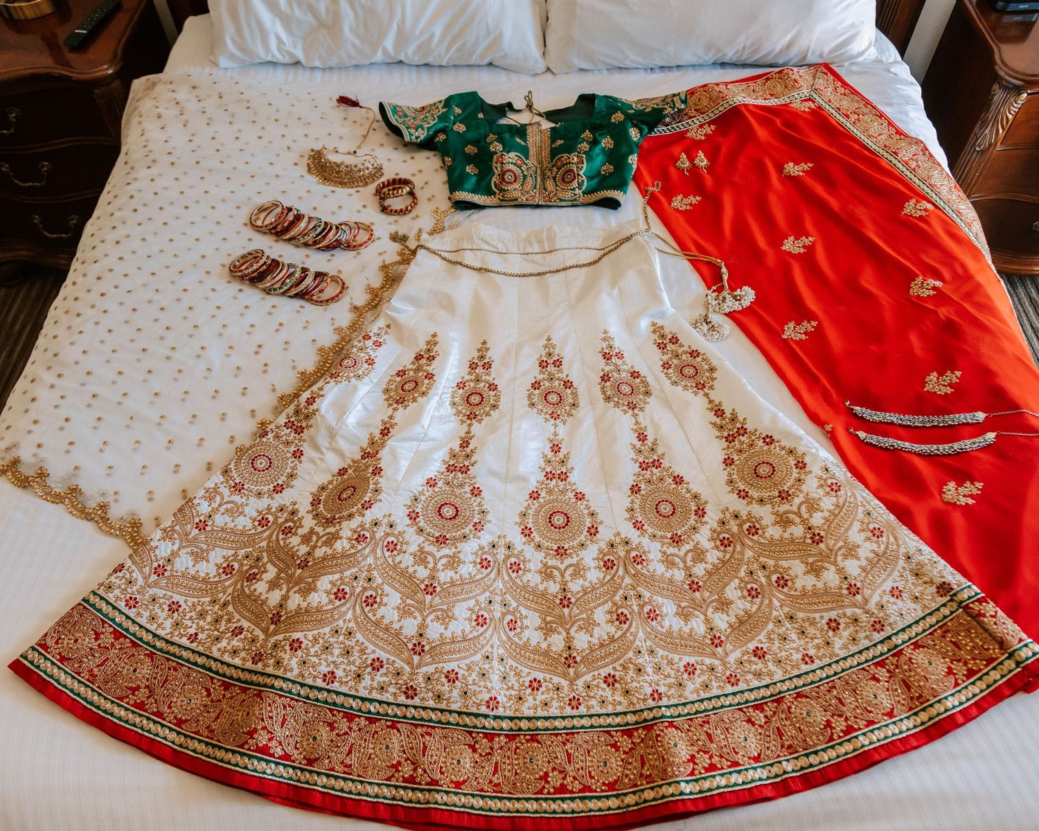 Elegant white and red bridal lehenga with gold embroidery laid flat on bed.