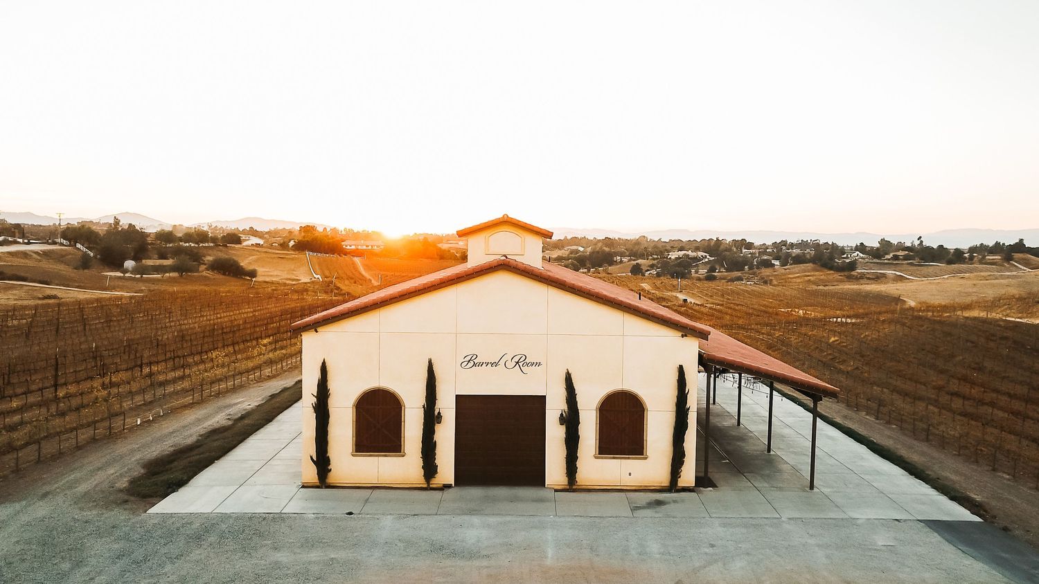 Sunset view of Barrel Rose winery building surrounded by vineyard rows in a scenic wine country landscape.