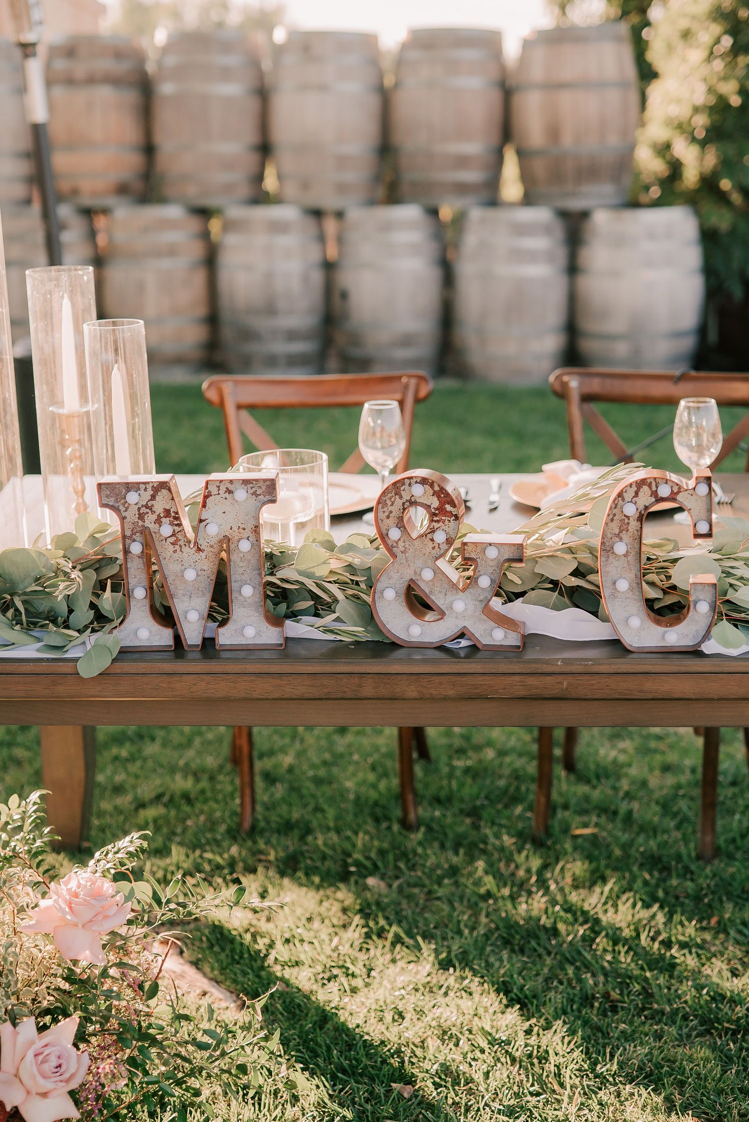 Rustic wedding sweetheart table with marquee initials M&G, greenery, and wine barrel backdrop.