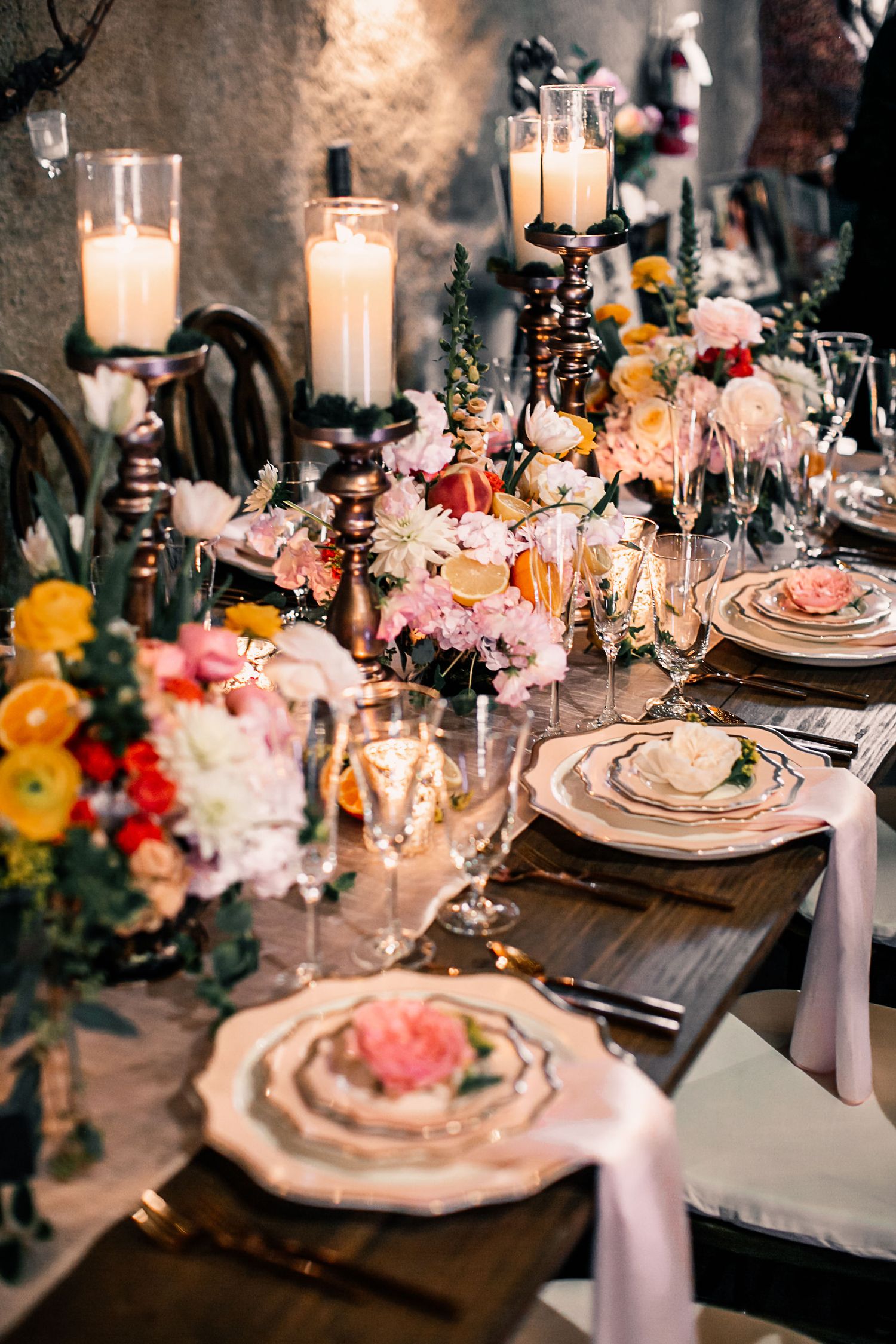 Elegant wedding tablescape with colorful floral centerpieces, white pillar candles, champagne flutes, and layered gold-rimmed plates.