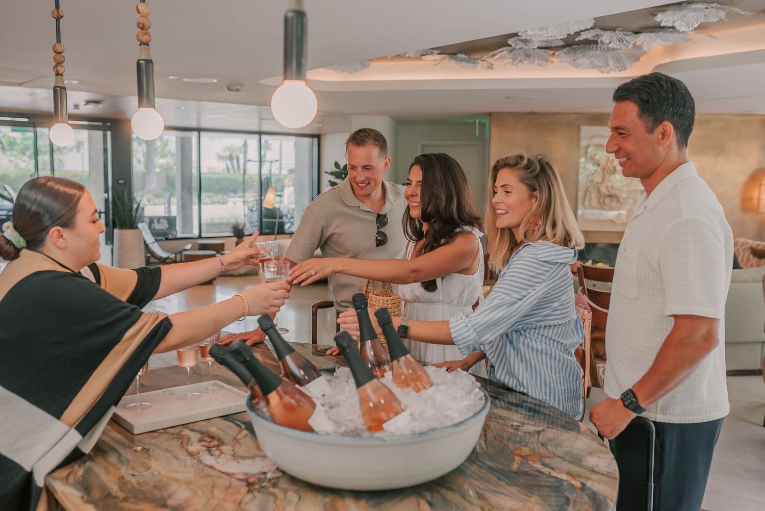 Staff serving champagne bottles on ice to guests at an elegant hotel bar reception area.