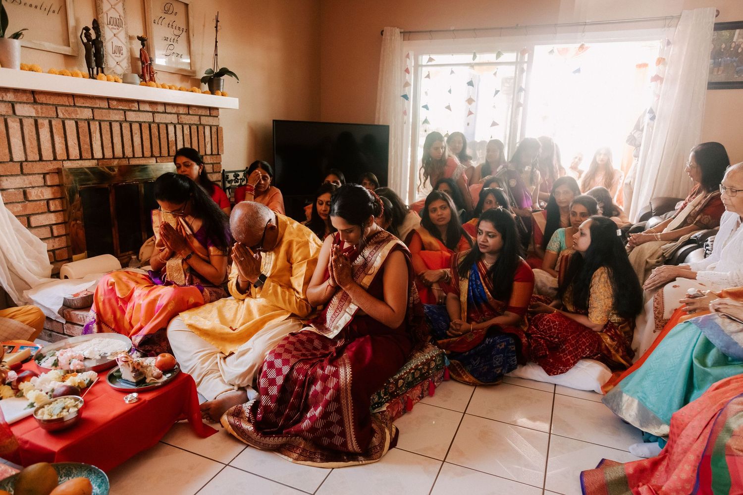 Guests in vibrant sarees sitting on floor during traditional Indian wedding ceremony indoors.