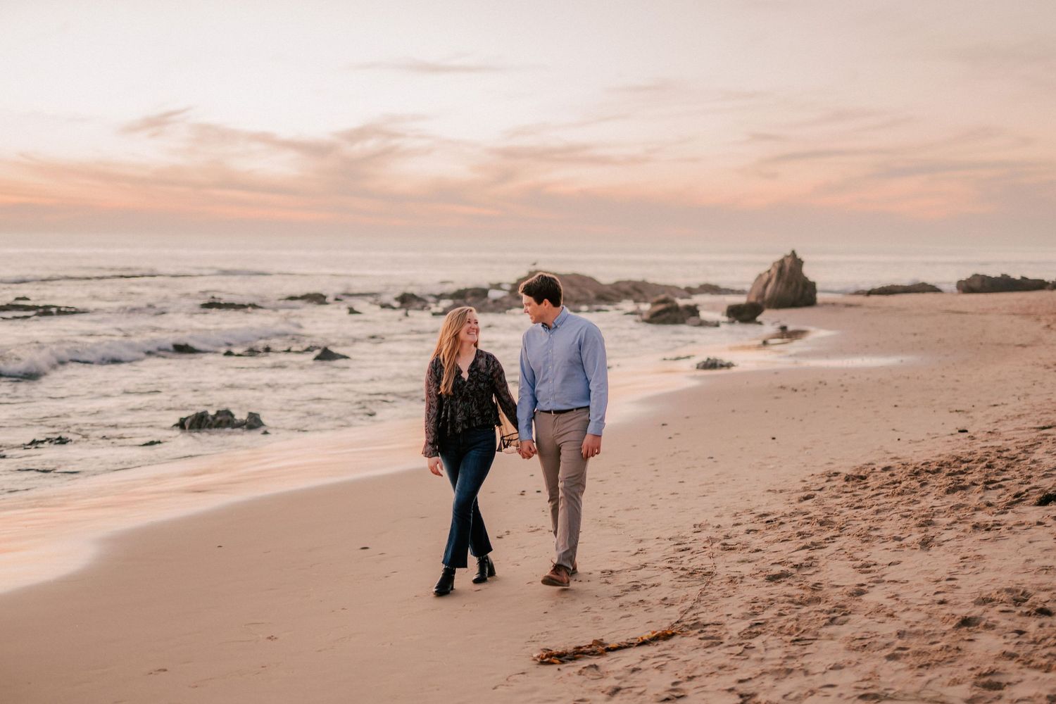 Happy couple strolling along scenic beach shoreline at golden sunset holding hands.