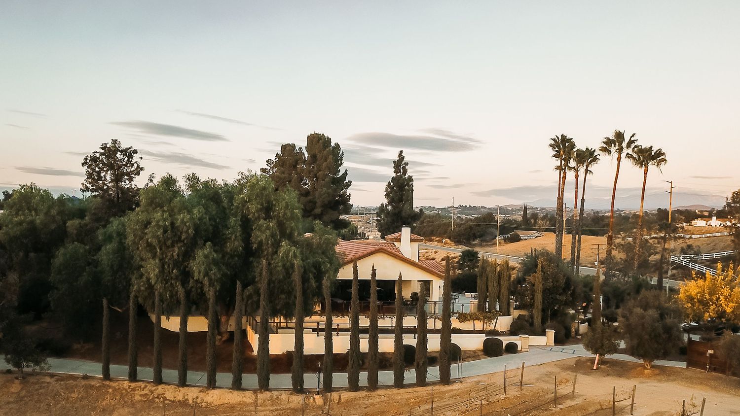 Aerial view of a Spanish-style home surrounded by palm trees and lush greenery at dusk in Southern California.