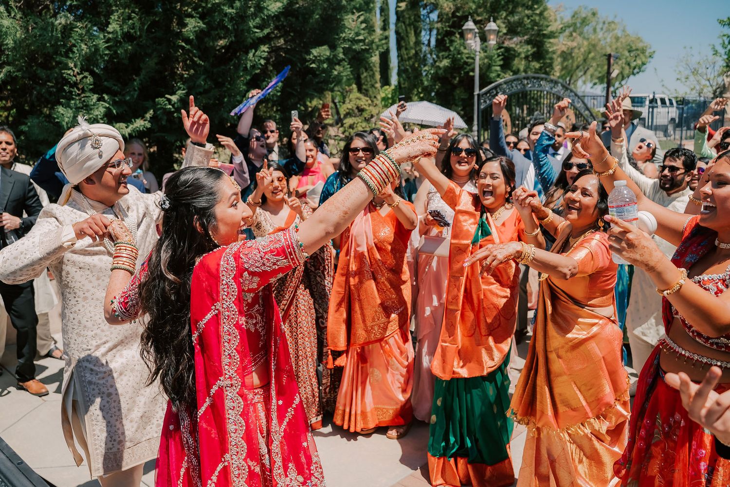 Indian wedding baraat celebration with bride in red lehenga dancing joyfully with guests in vibrant traditional attire.