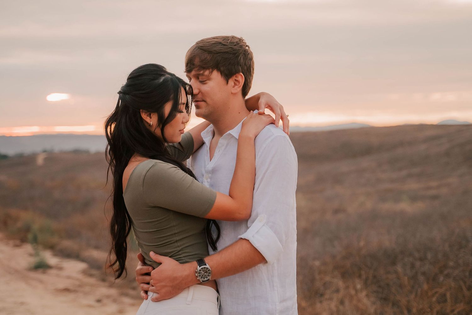 Couple embracing at sunset in a scenic desert landscape, sharing a romantic moment with golden sky backdrop.