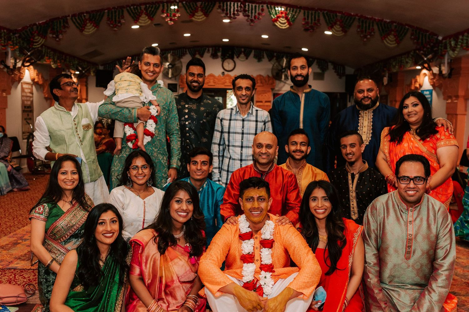 Large group of guests in traditional Indian attire posing with the groom at a Hindu wedding celebration.