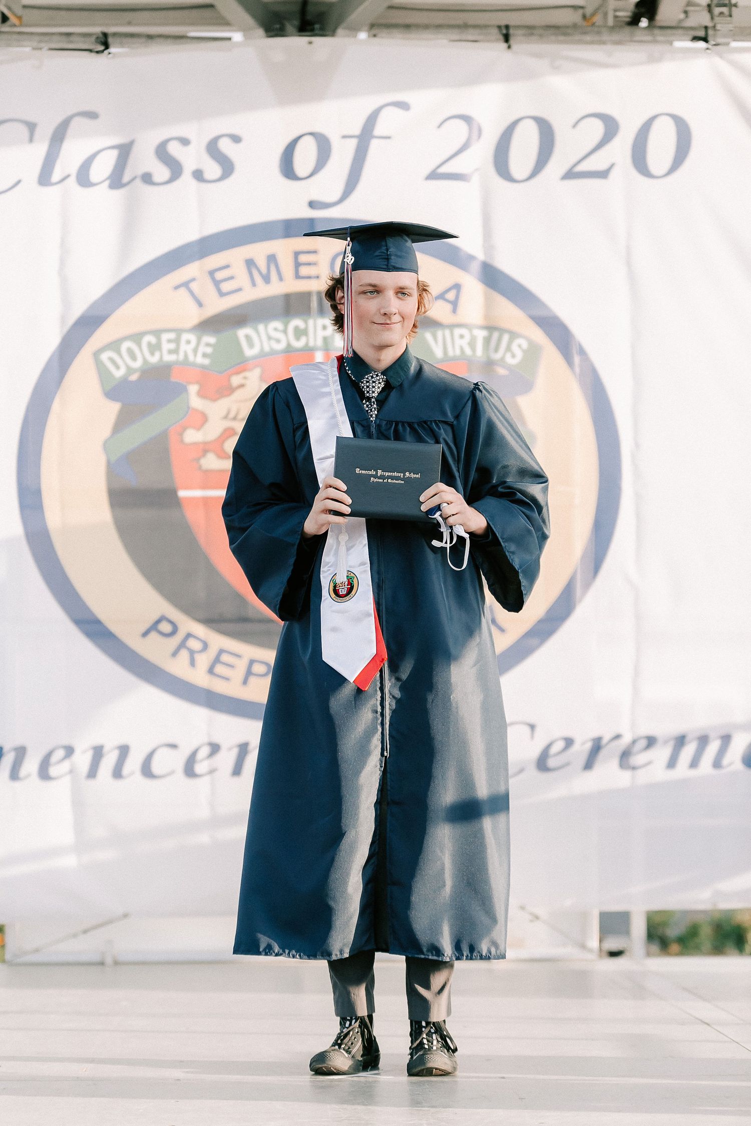 A graduate in navy cap and gown holds diploma at Temecula Prep Class of 2020 commencement ceremony.