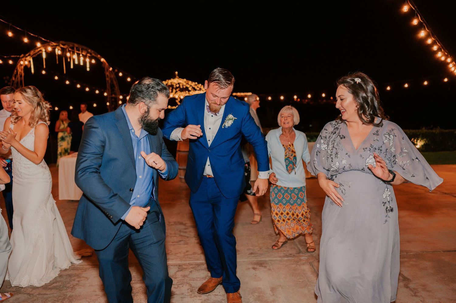Wedding guests dancing outdoors at night under string lights at a festive reception celebration.