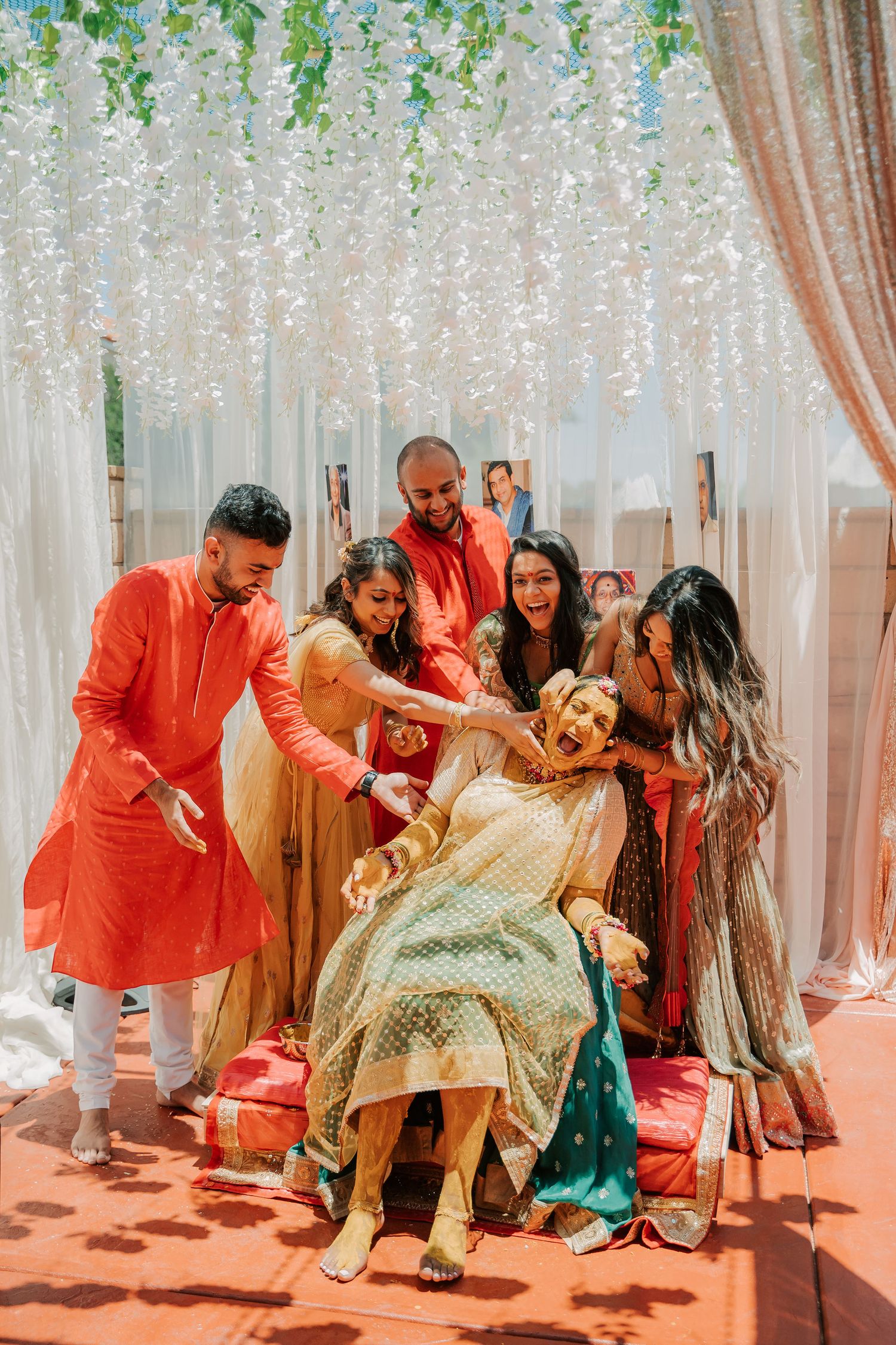 Friends playfully apply haldi turmeric paste on laughing bride during Indian wedding ceremony.