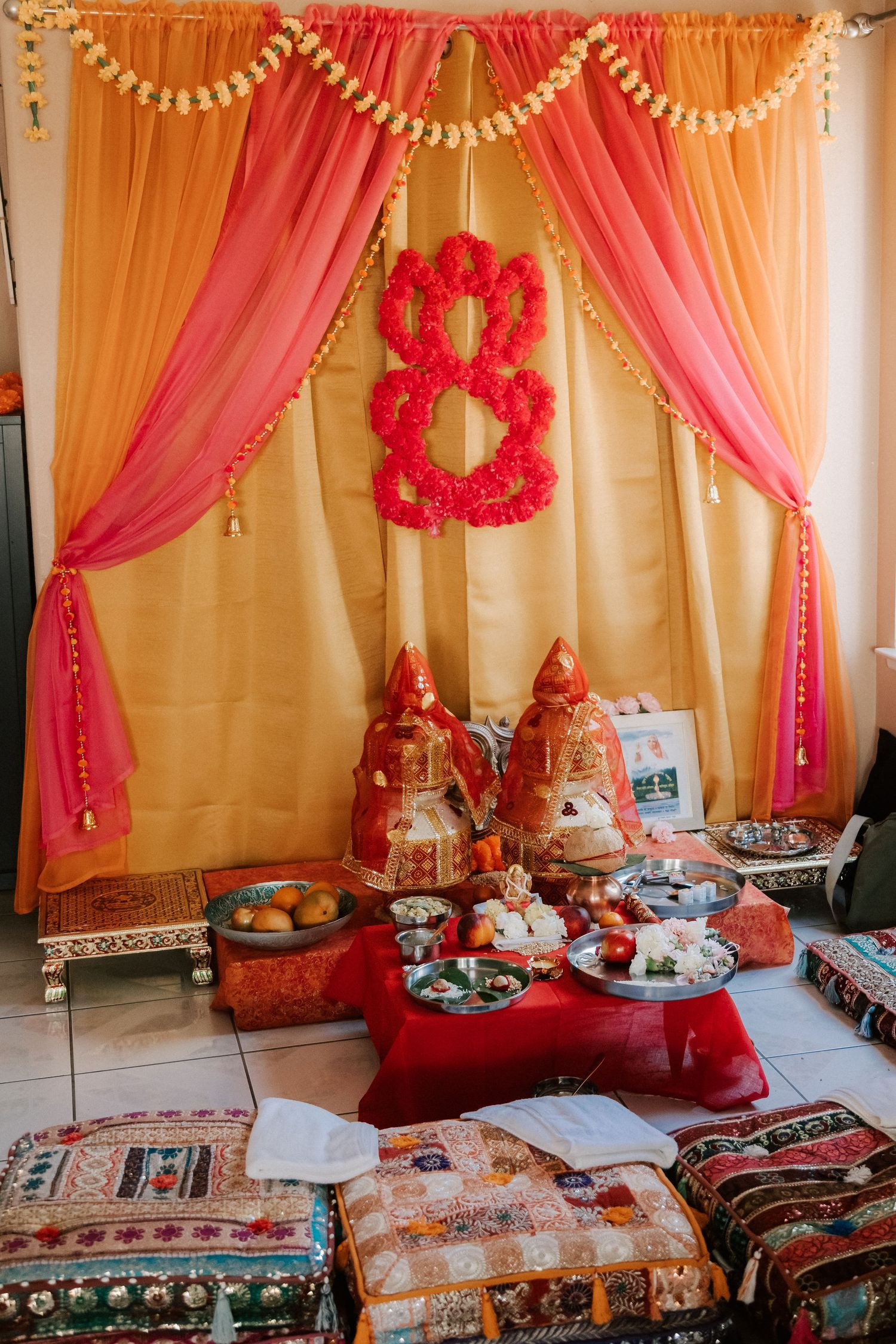 Colorful Indian wedding mandap decorated with orange pink drapes and red floral arrangements.