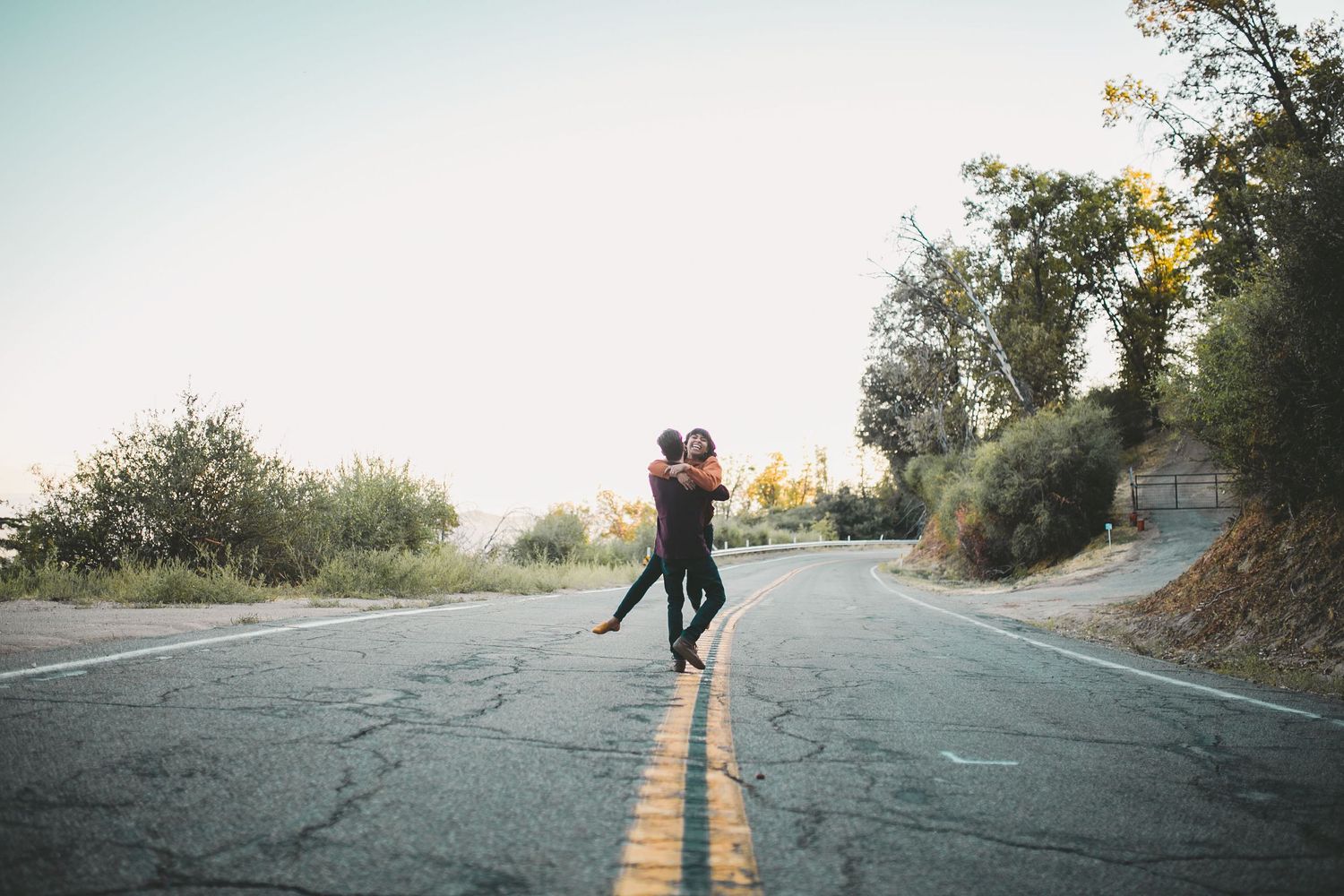 Couple embracing and dancing on an empty road surrounded by trees during golden hour.