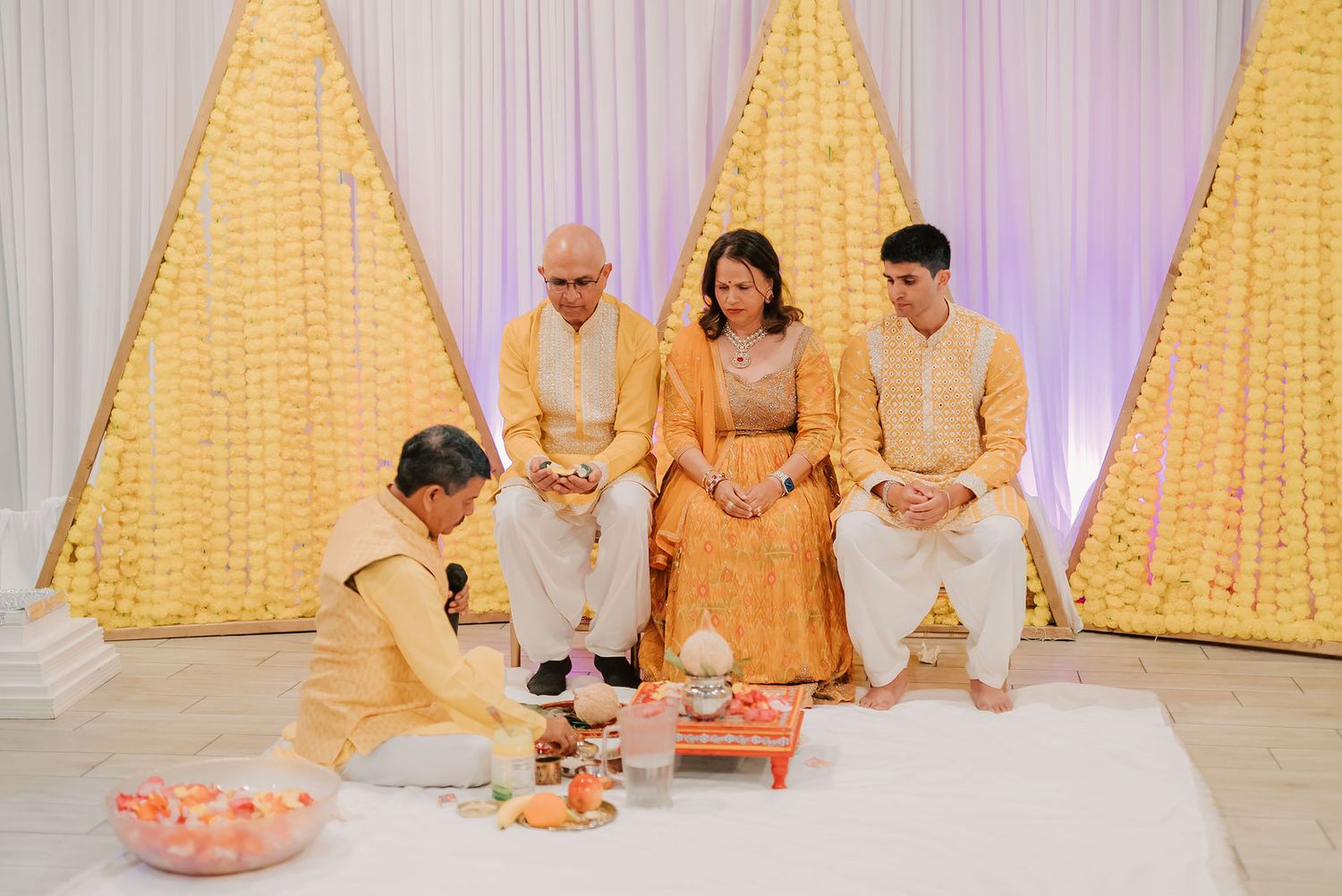Family gathered for an Indian Hindu wedding ceremony with yellow floral backdrop and traditional attire.