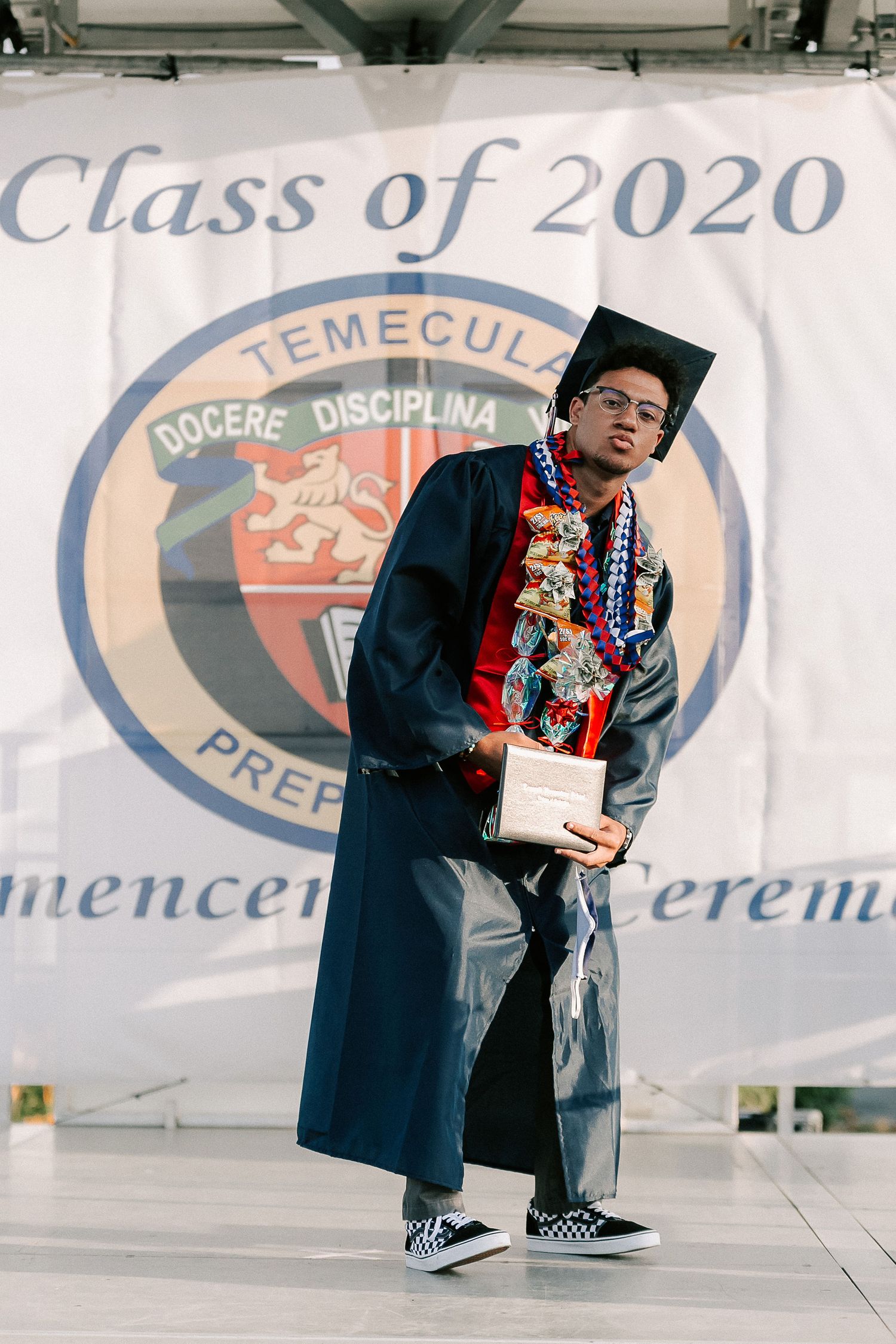 A decorated graduate poses proudly in cap and gown at Temecula Prep Class of 2020 graduation ceremony.