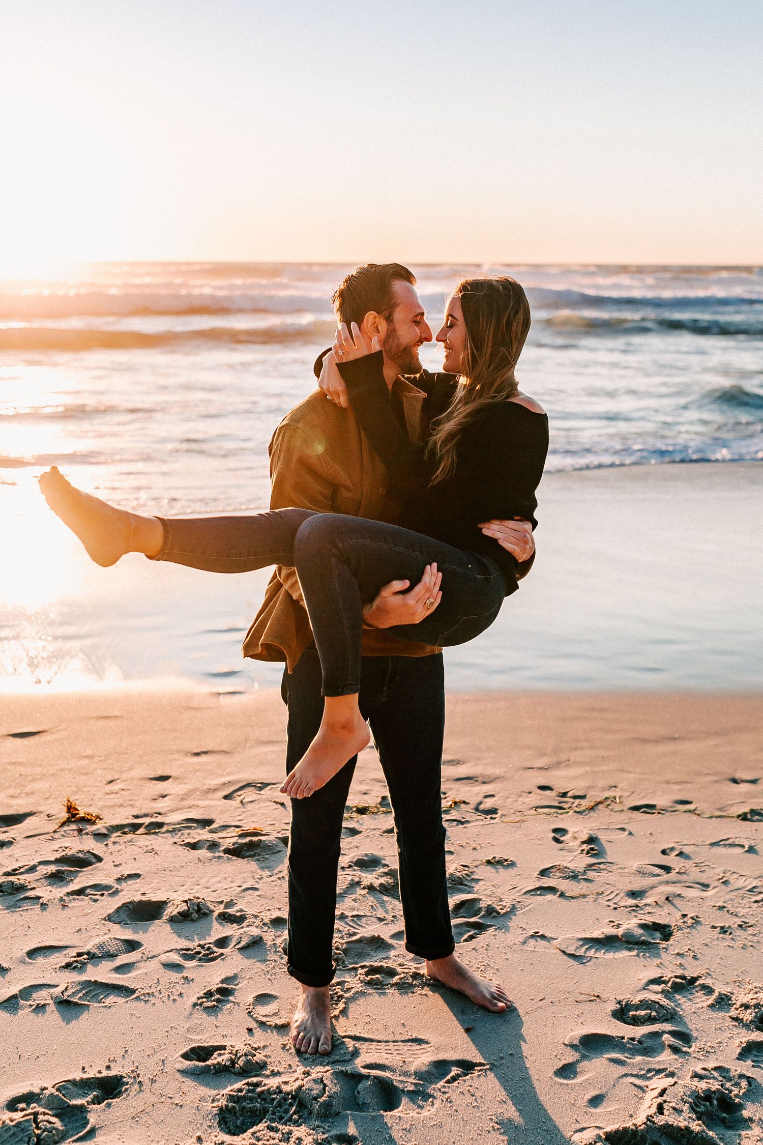 Man carrying woman in his arms on beach at sunset, couple sharing a romantic kiss.