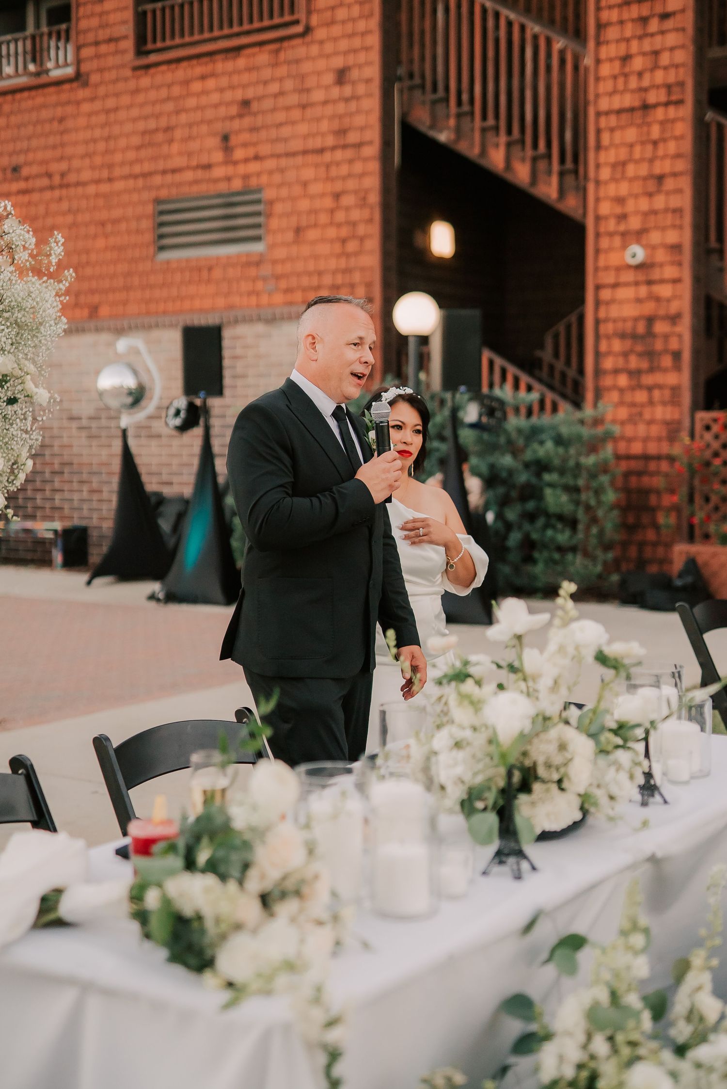 Bride and groom sharing a toast at an elegant outdoor wedding reception with white floral centerpieces.