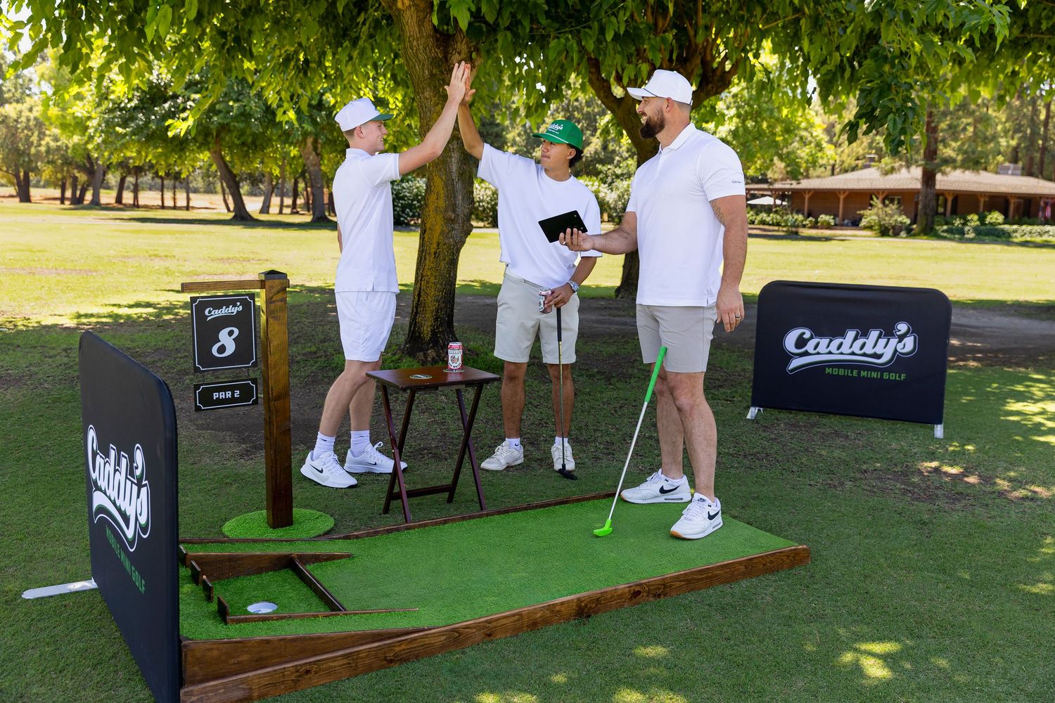 Three people high-fiving at Caddy's Mobile Mini Golf station 8 on a sunny golf course.