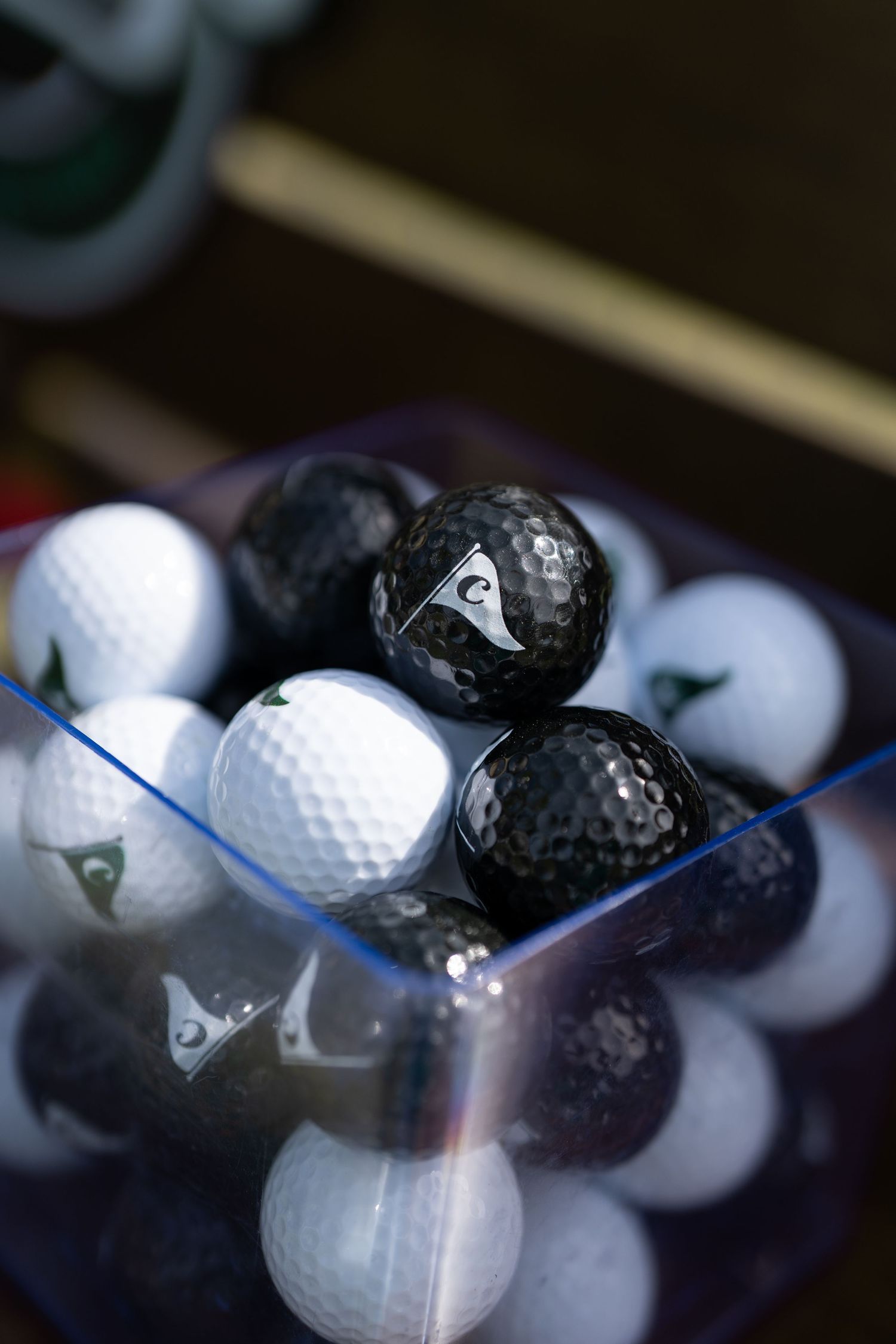 Black and white branded golf balls displayed in a clear square container at a mini golf event.