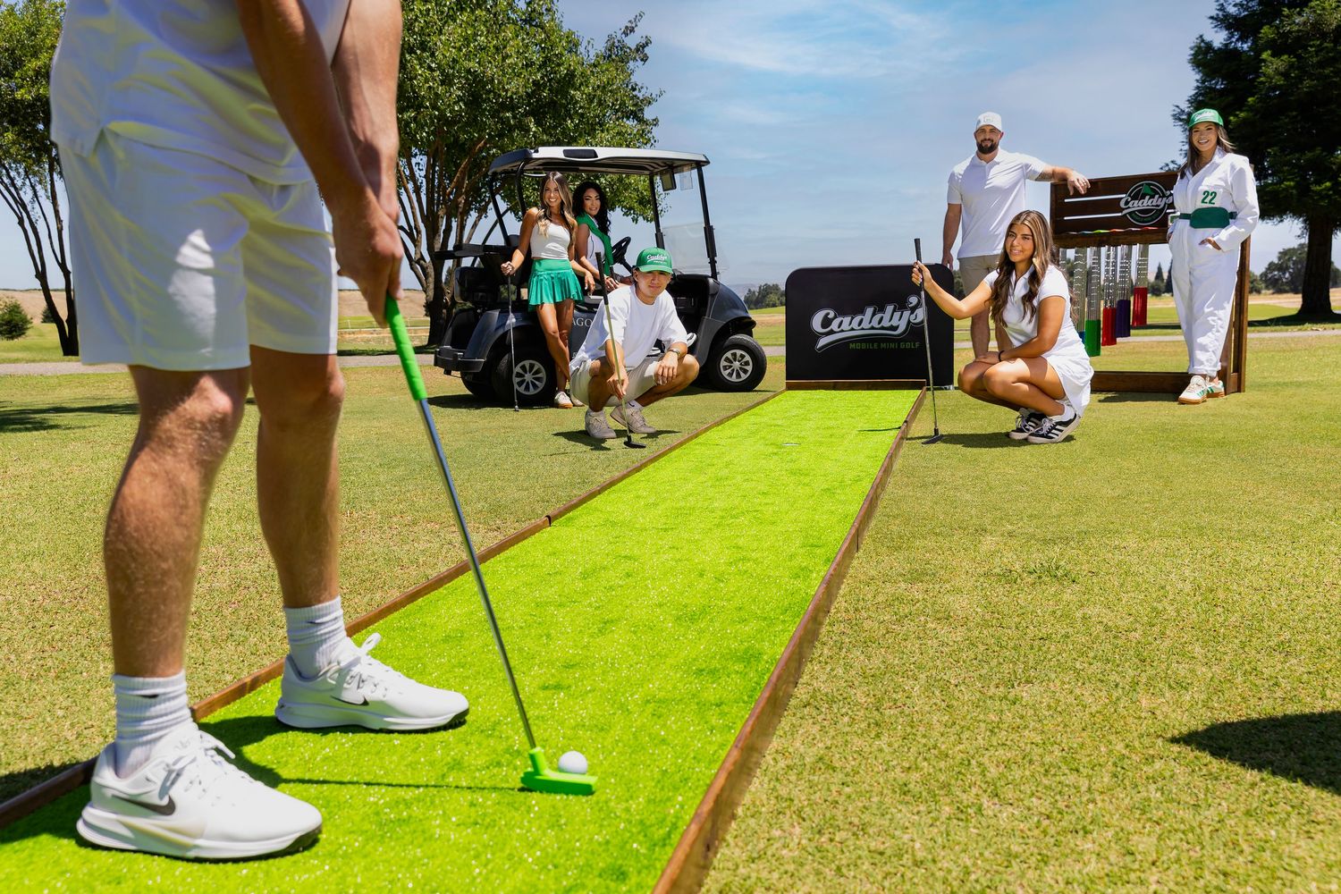 Golfers practicing putting on a green course near a golf cart on a sunny day.