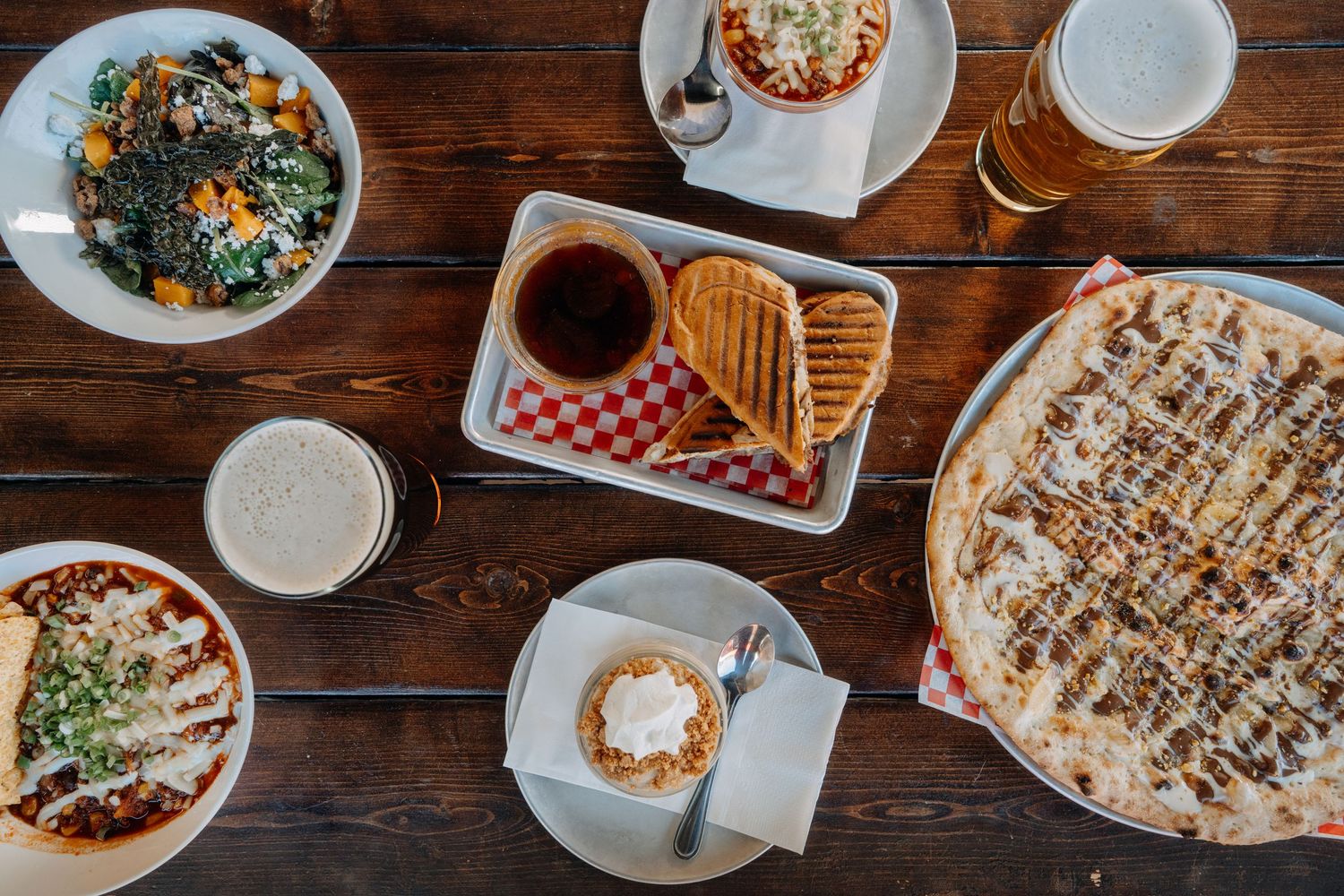 Overhead shot of cocktails, salads and wood-fired pizza — restaurant photography for Kelowna dining scene by James Fujita.