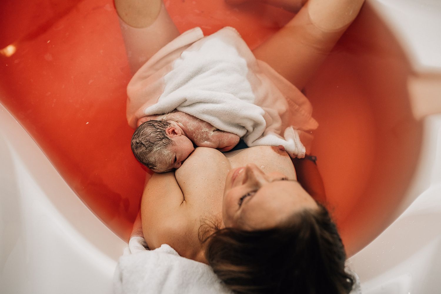 relieved smiling mother holding her newborn in a bathtub during a birth photo shoot in Dubai