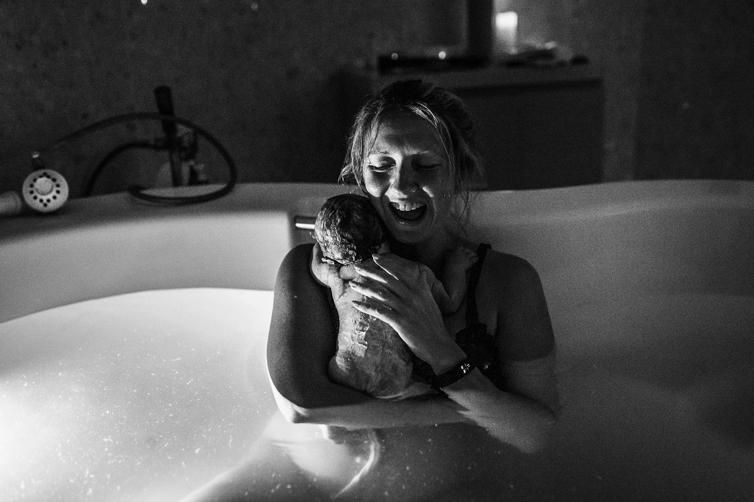 smiling mom holding her new baby in a bathtub captured by gigi dubai birth photographer