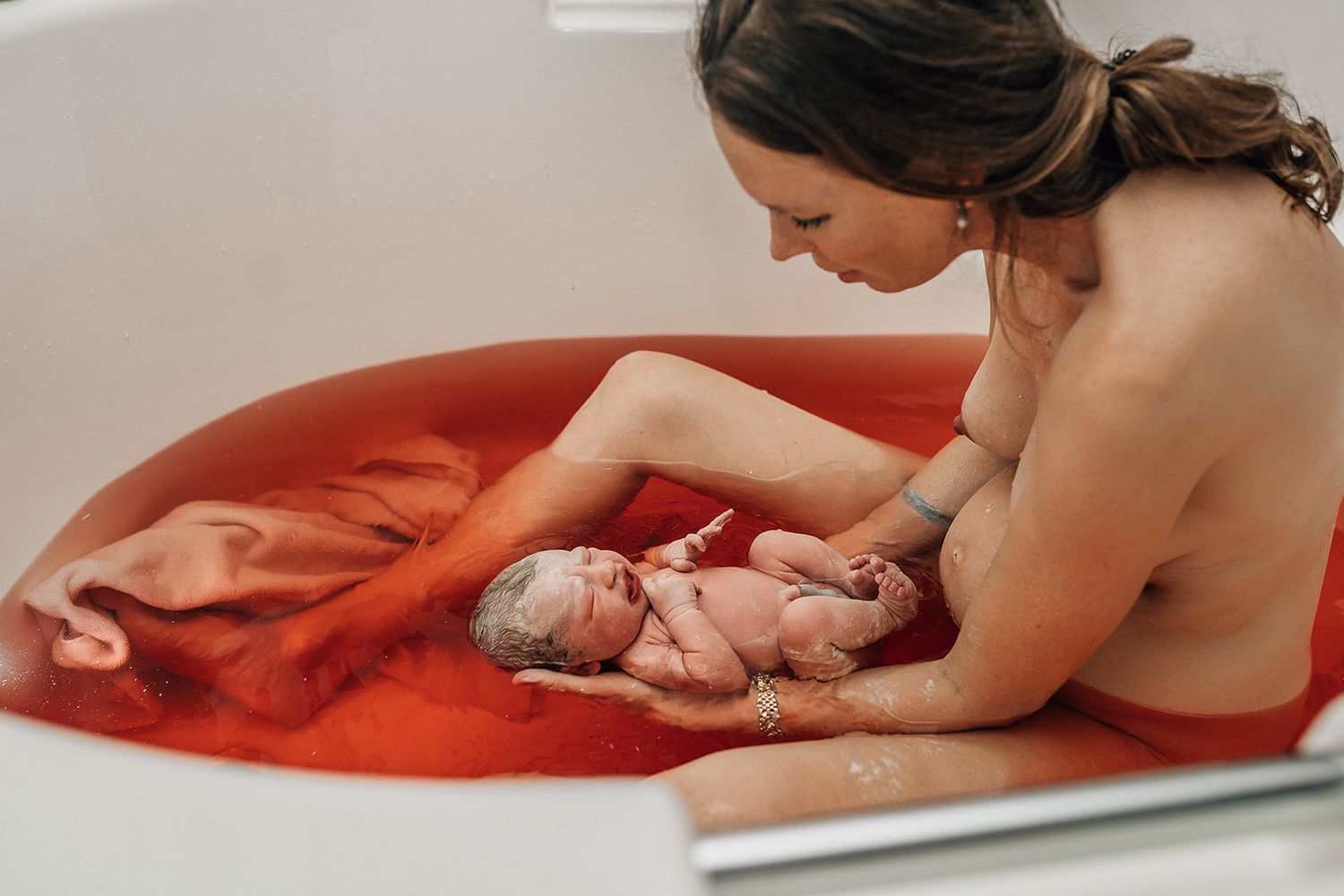 mom holding her newborn girl right after the birth during a water birth shoot in dubai