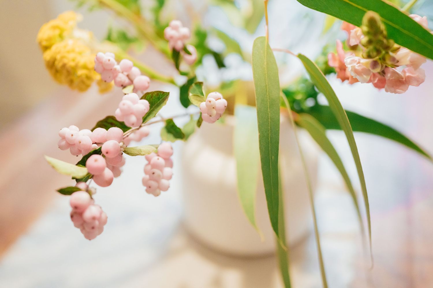 Soft pink and yellow floral arrangement with green stems in white vases on light background.