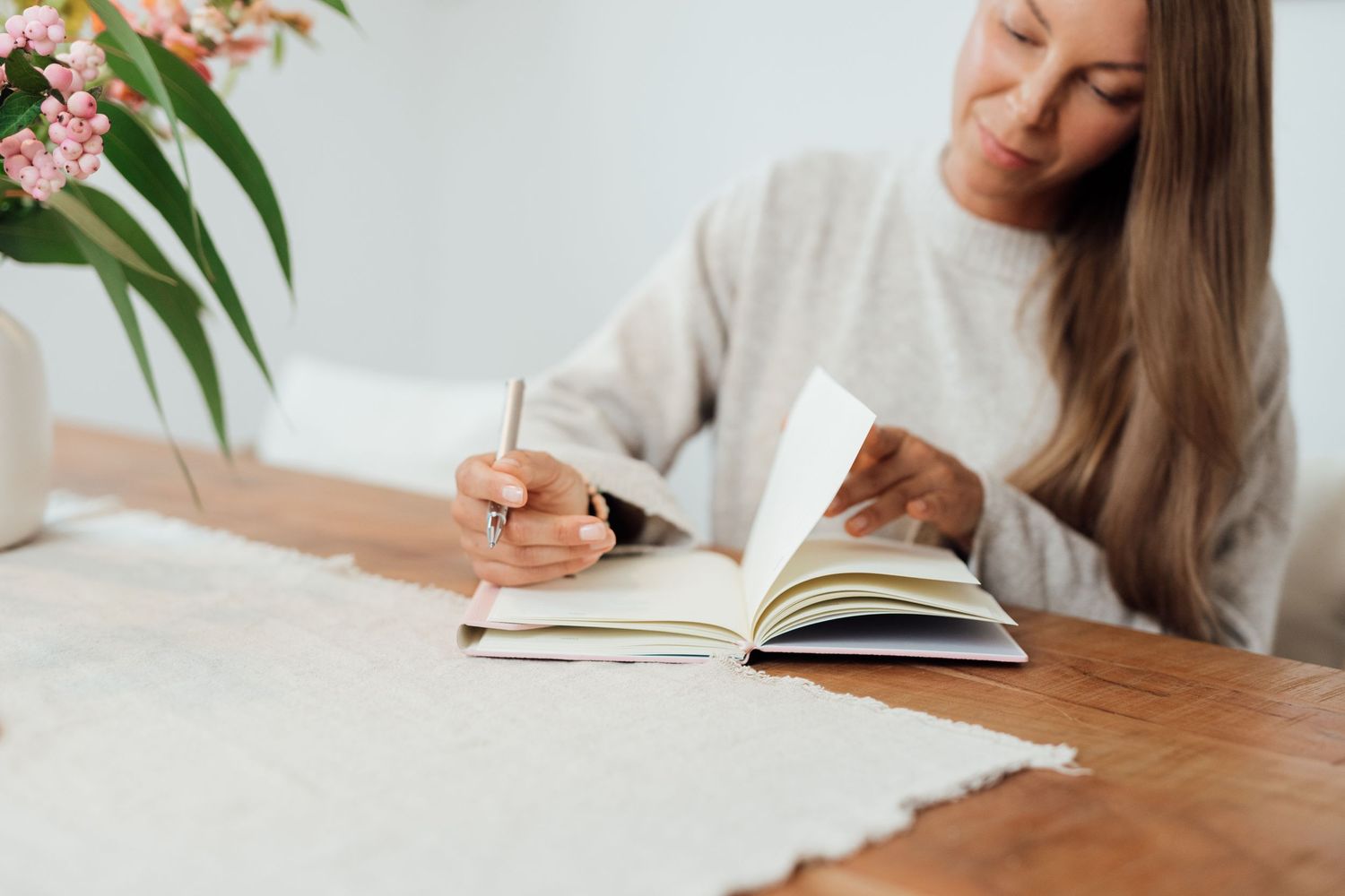 Woman writing in journal at wooden desk in bright minimalist setting.
