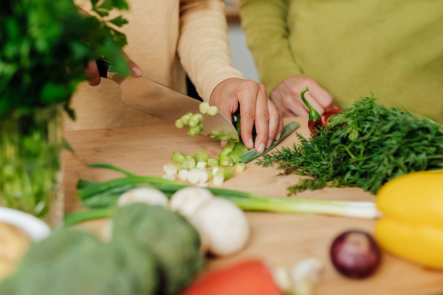 Fresh vegetables being chopped on wooden cutting board in bright kitchen.