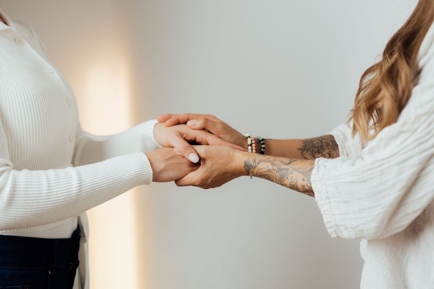Two people holding hands in supportive gesture wearing white sweaters.
