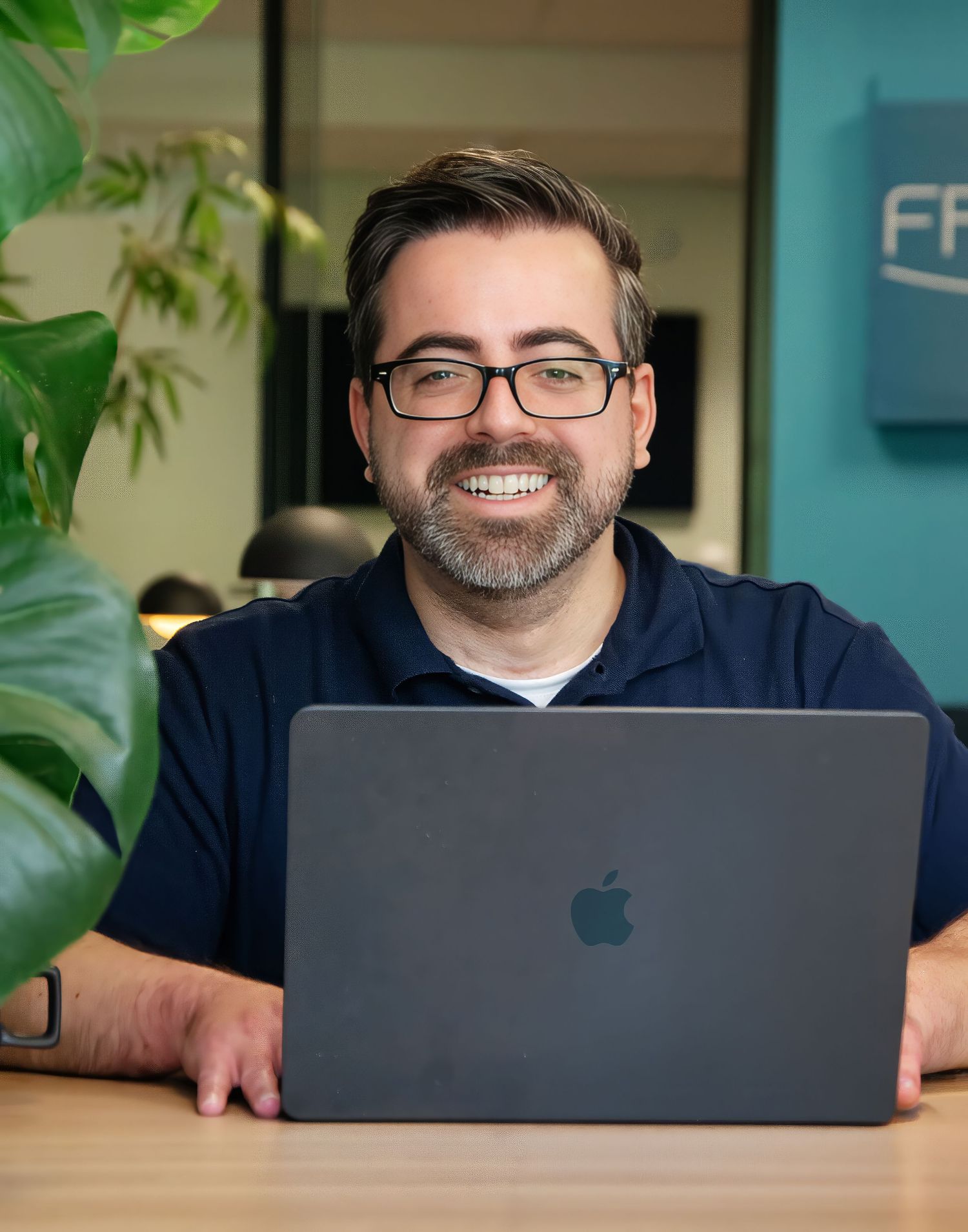 Personal branding portrait of a smiling male entrepreneur working on a laptop in a modern workspace in Rotterdam.