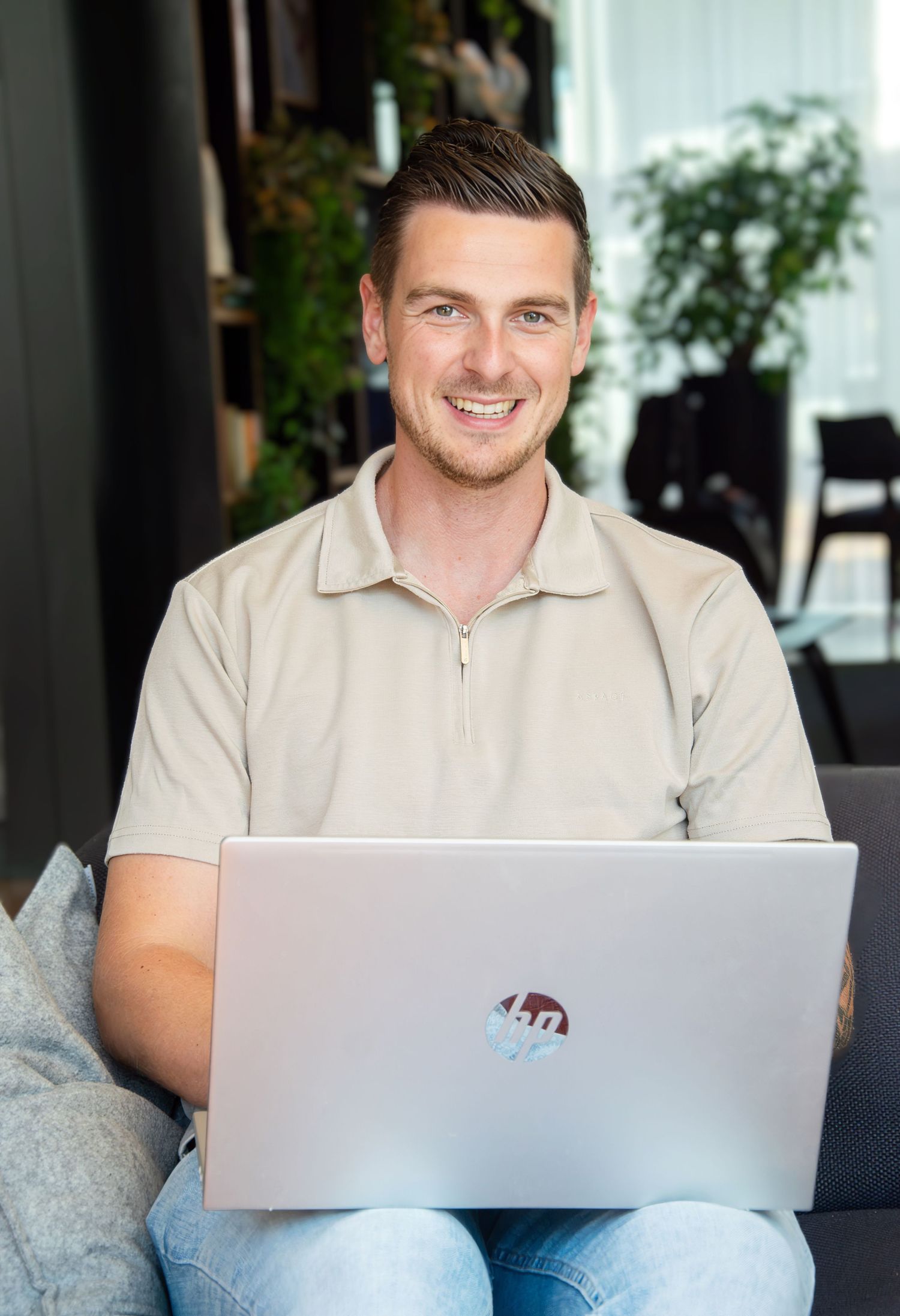 Personal branding portrait of a smiling male entrepreneur working with a laptop in a relaxed modern setting in Rotterdam.
