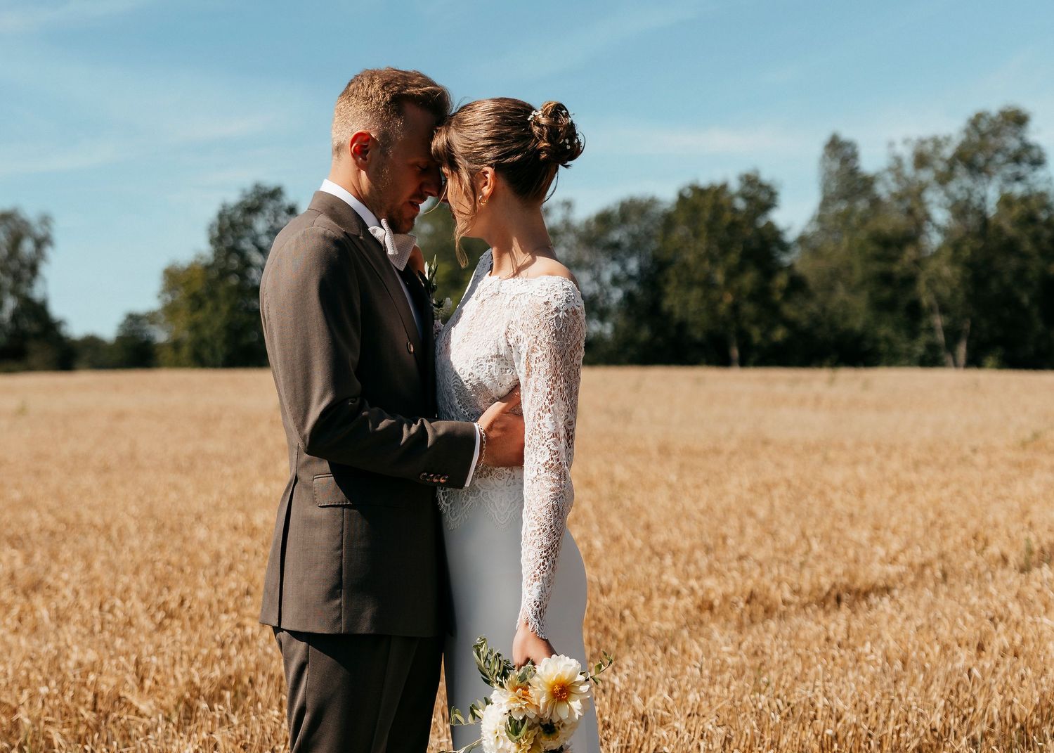 Newlyweds share intimate moments while standing in a sun-lit wheat field.