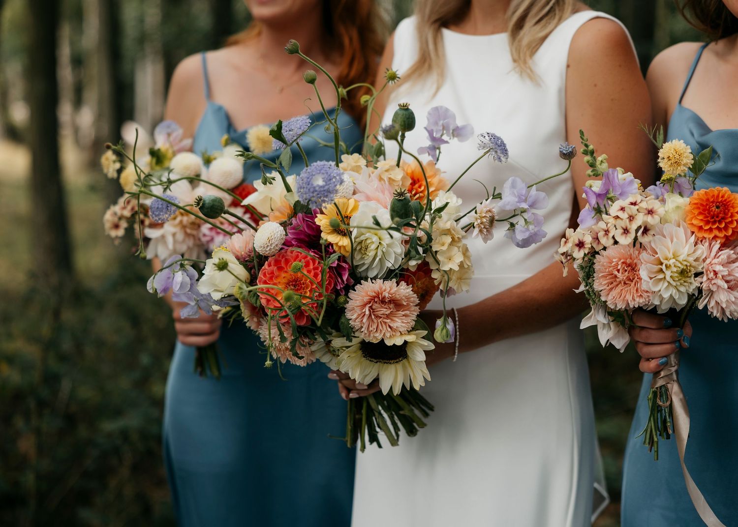 Wedding party members hold colorful bouquets with sunflowers and mixed florals against navy blue dresses.