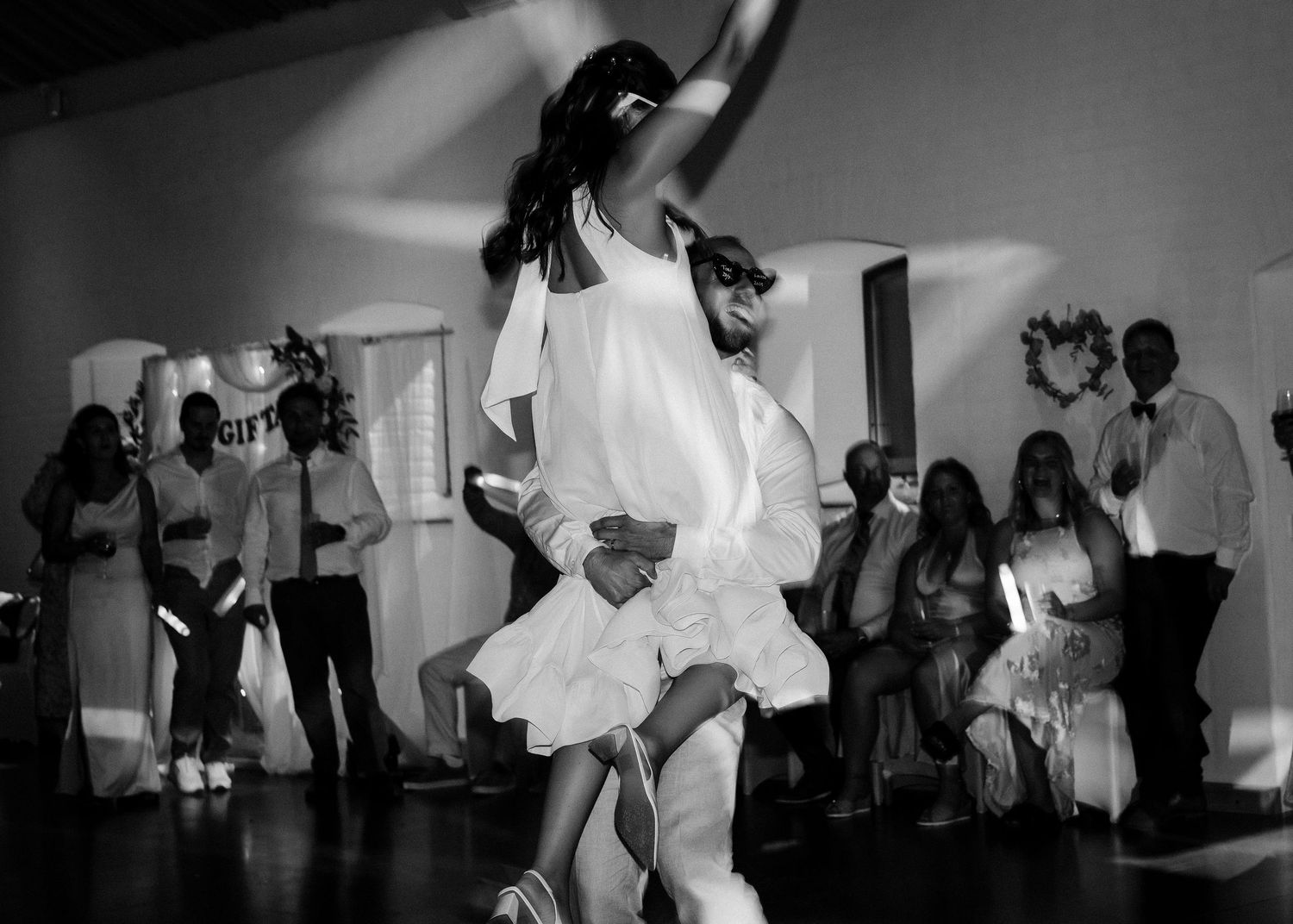 Black and white photo of wedding guests dancing energetically at a reception.