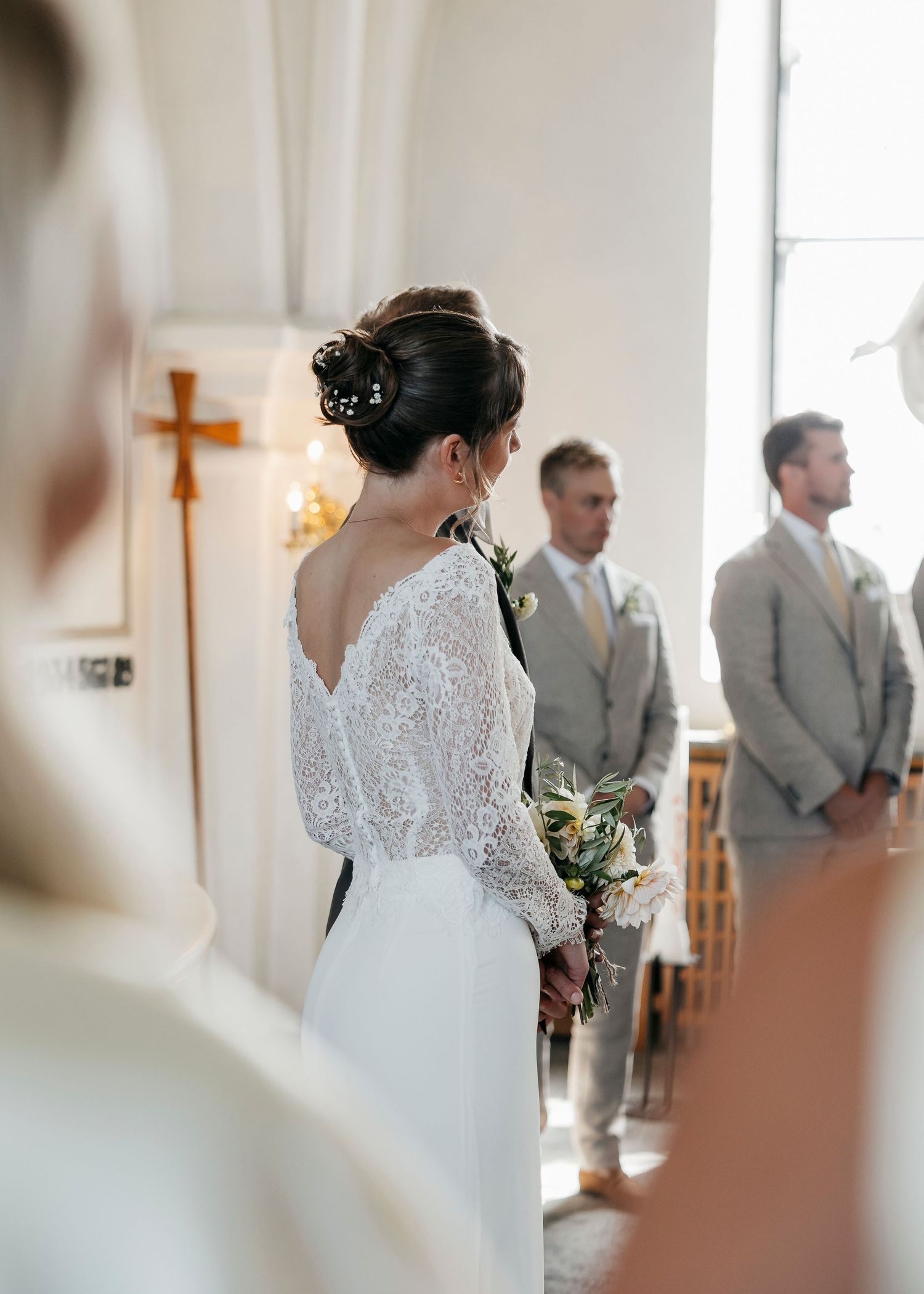 Elegant wedding ceremony in a bright white church with groomsmen in grey suits.