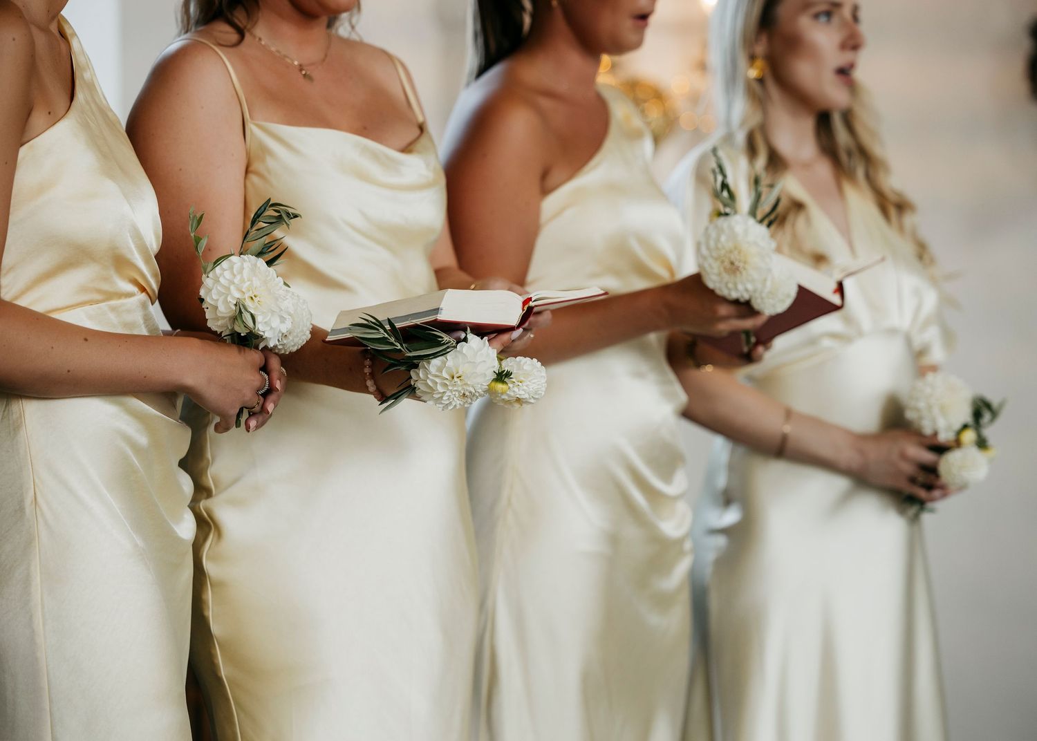 Row of bridesmaids in pale yellow dresses holding white floral bouquets.