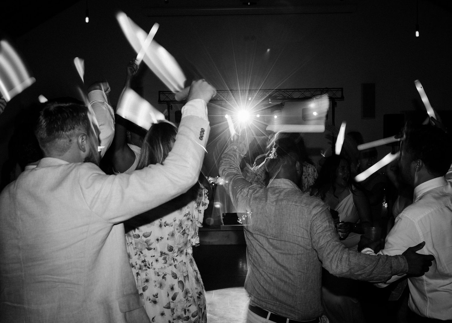 Black and white photo of wedding guests dancing with light sticks creating streaks of light.