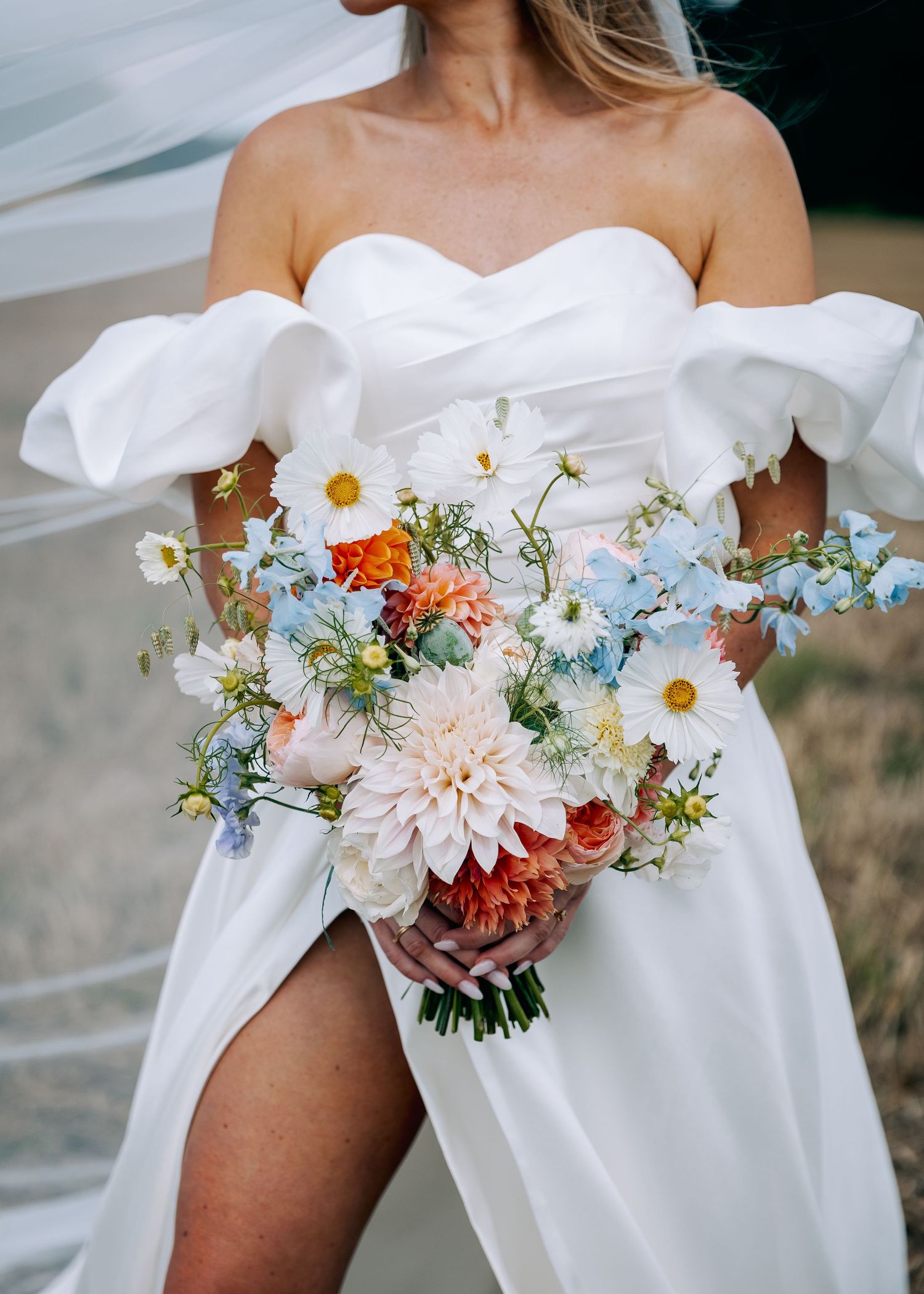 Close-up of bridal bouquet with daisies and summer flowers against white dress.