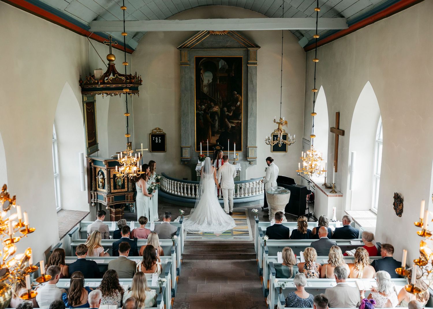 Panoramic view of a church wedding ceremony with guests seated in wooden pews.