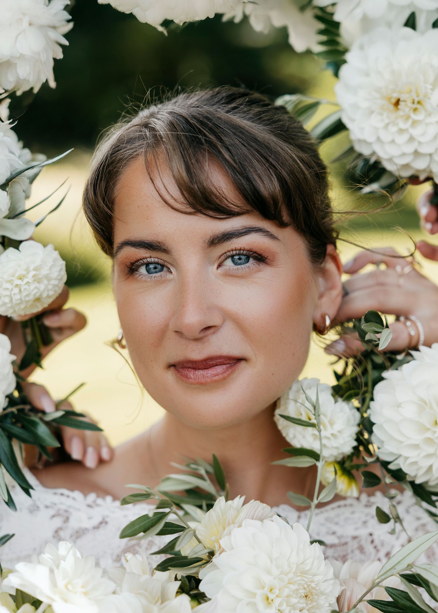 Bridal portrait framed by white flowers and greenery in natural lighting.