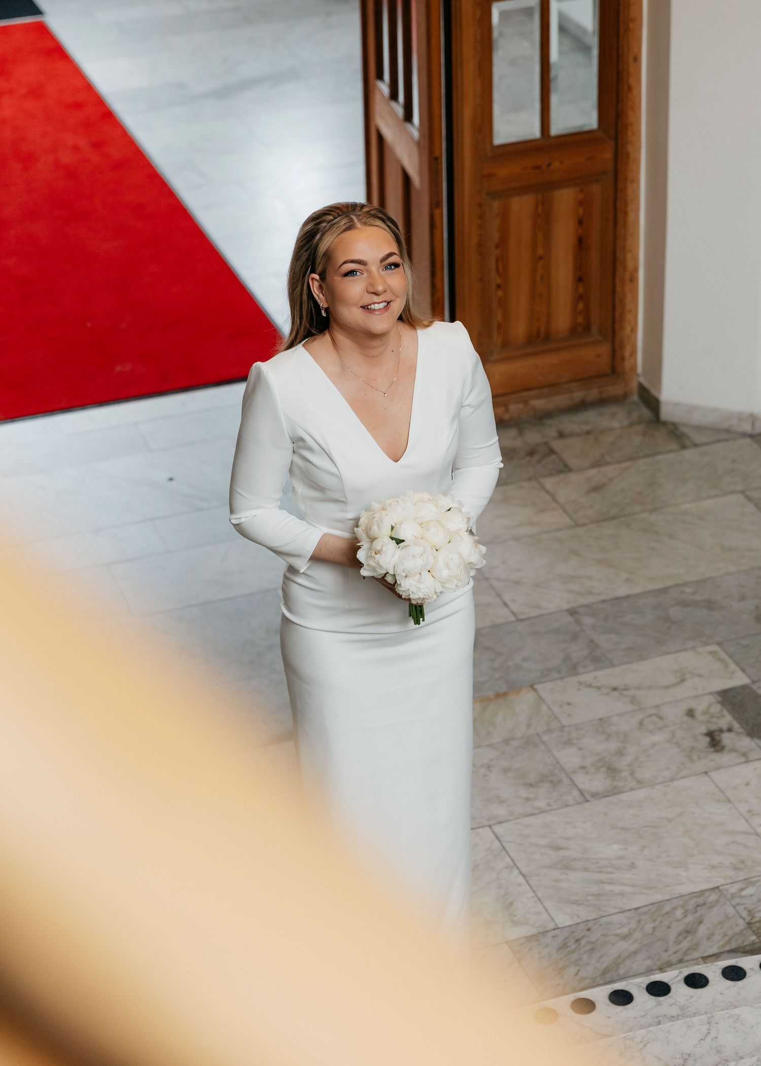 A bride in a modern white dress holds a bouquet of white flowers in an elegant indoor setting.