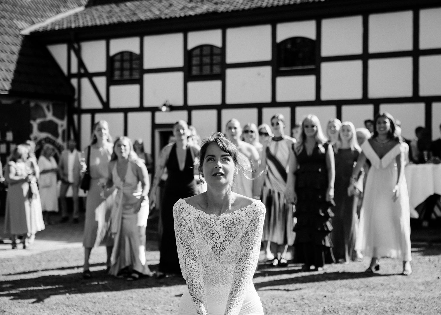 Wedding party and guests gathered outside a white and black timber-framed building.