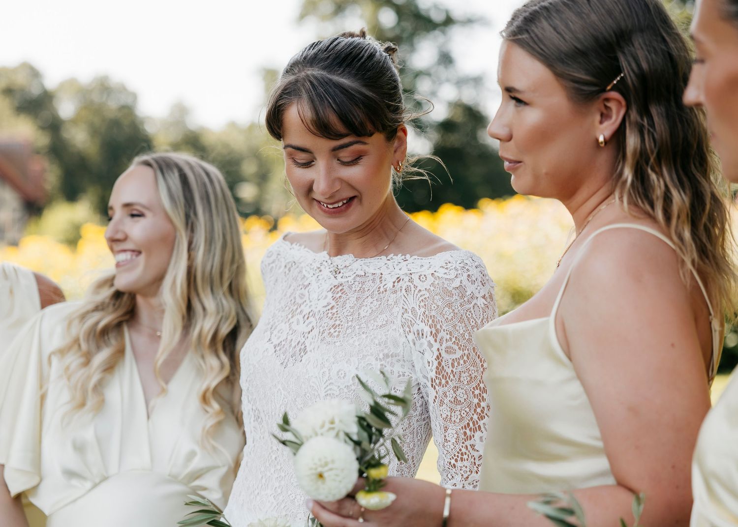 Bridesmaids in white dresses share candid moments during outdoor wedding celebration.