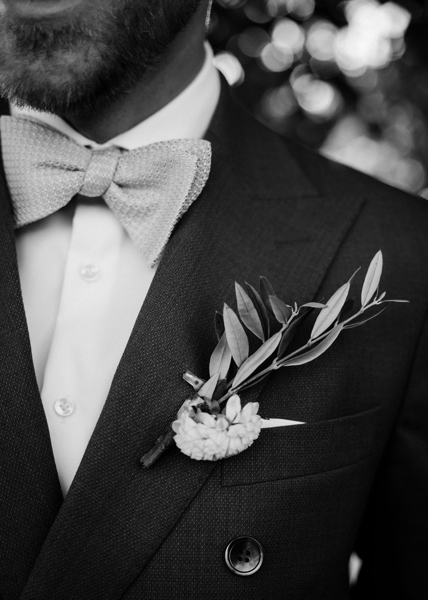 Close-up of groomsmen's boutonnieres with delicate white flowers and greenery against black suits.